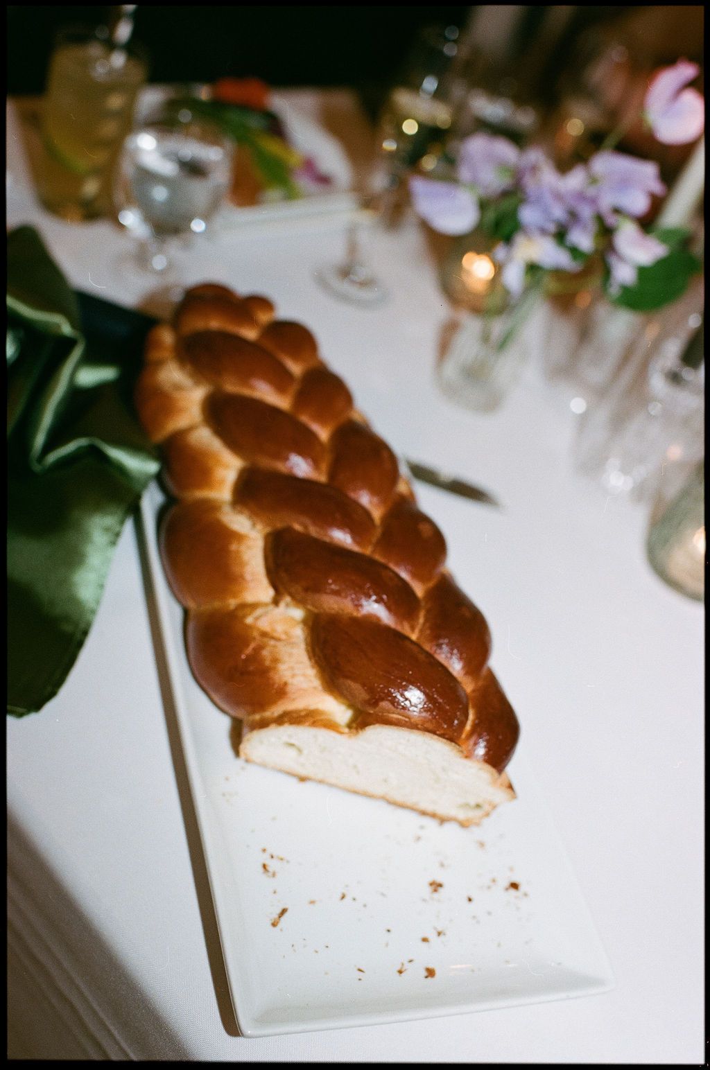 A beautifully braided challah bread loaf displayed on a white serving platter at a formal event.