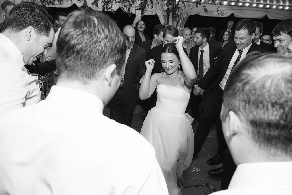 Black and white photo of wedding guests dancing and celebrating at a lively reception.