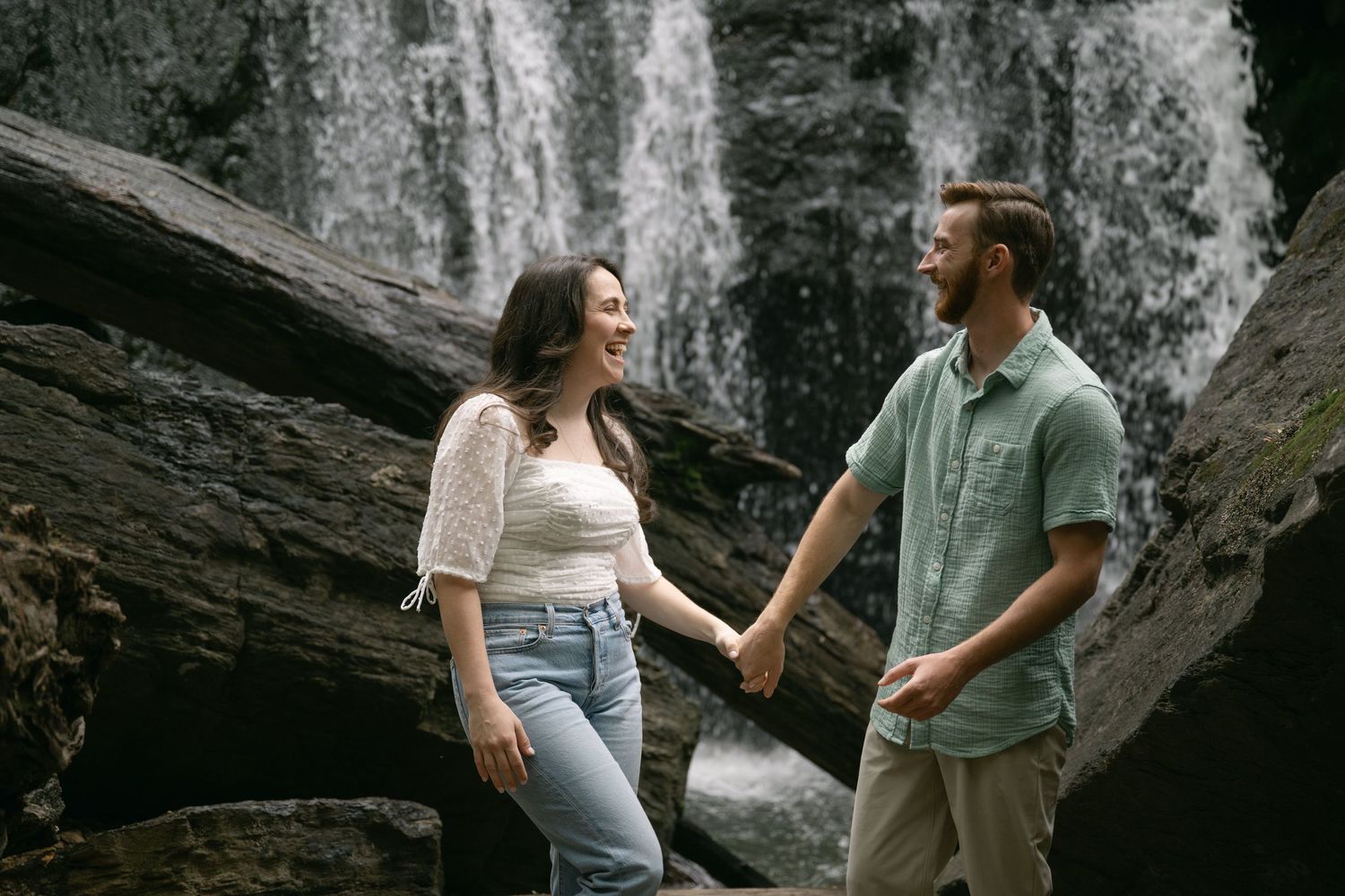 A romantic moment unfolds by a cascading waterfall in a forest setting.