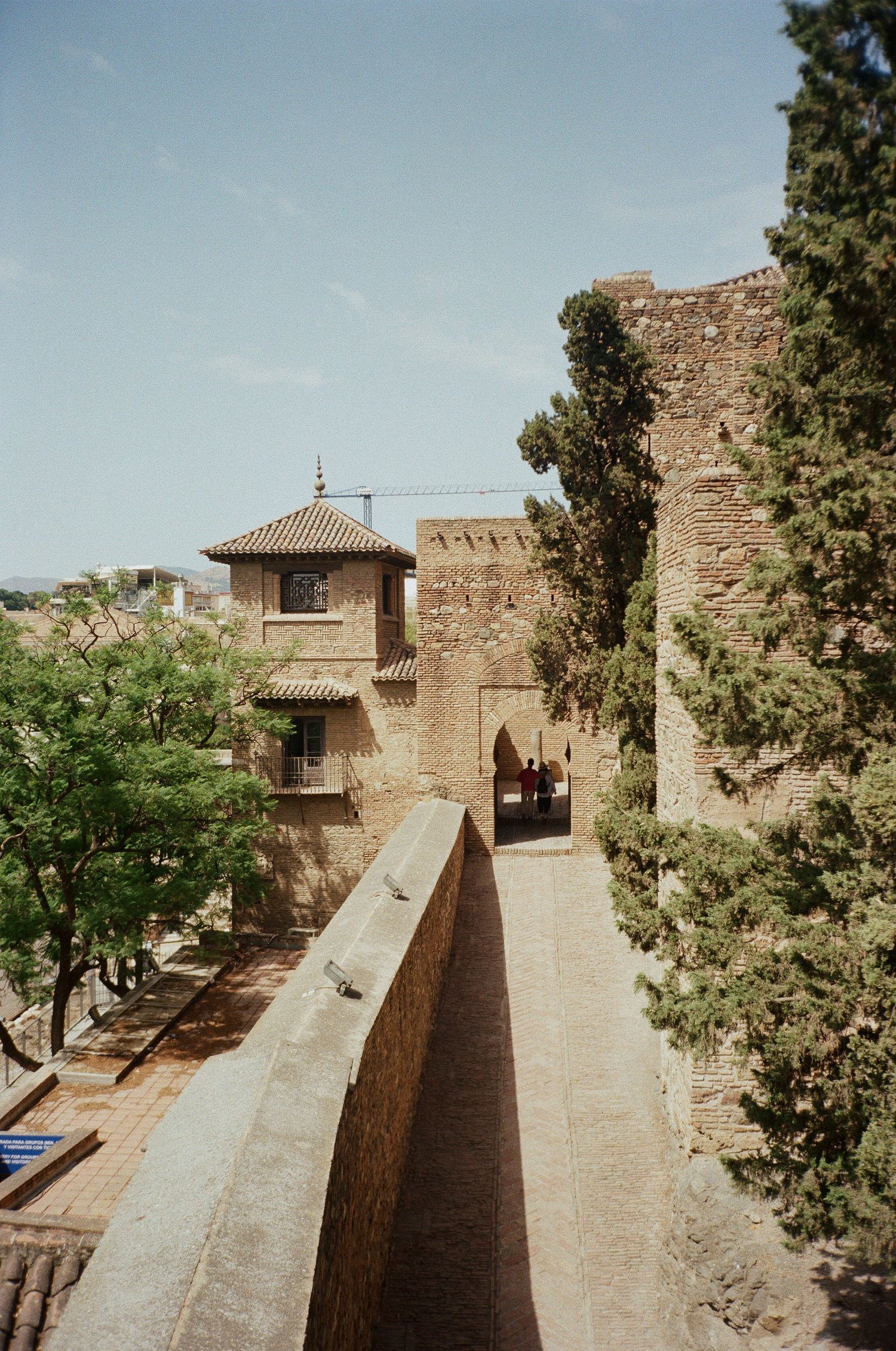 Ancient stone fortress wall and walkway with cypress trees and traditional Spanish architecture.