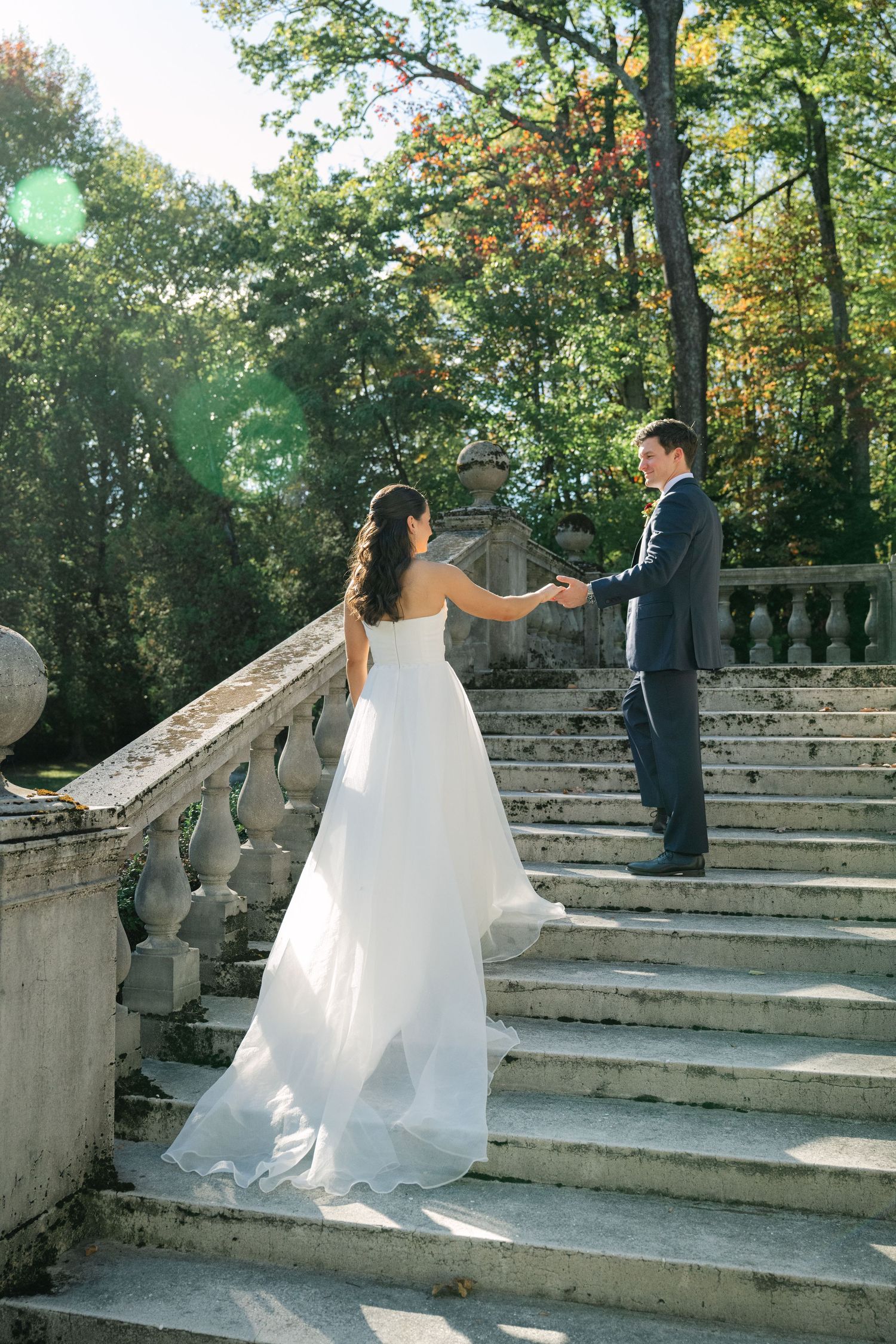 A couple poses on elegant stone steps in a garden setting during a wedding photo session.