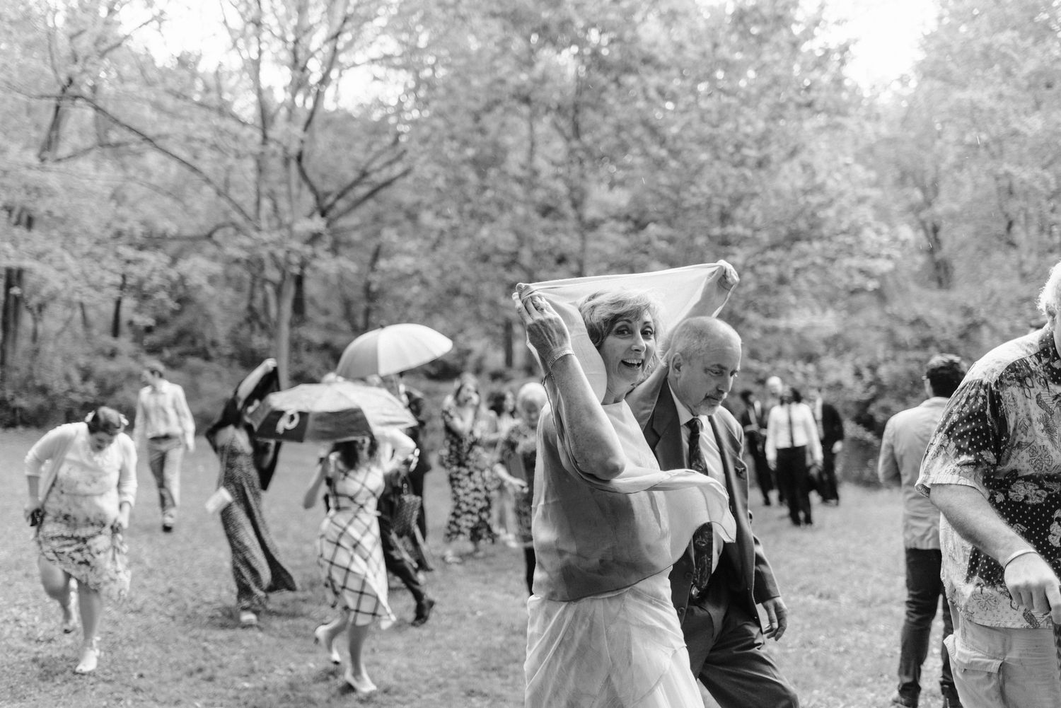 Wedding guests gather outdoors under umbrellas on a rainy day.