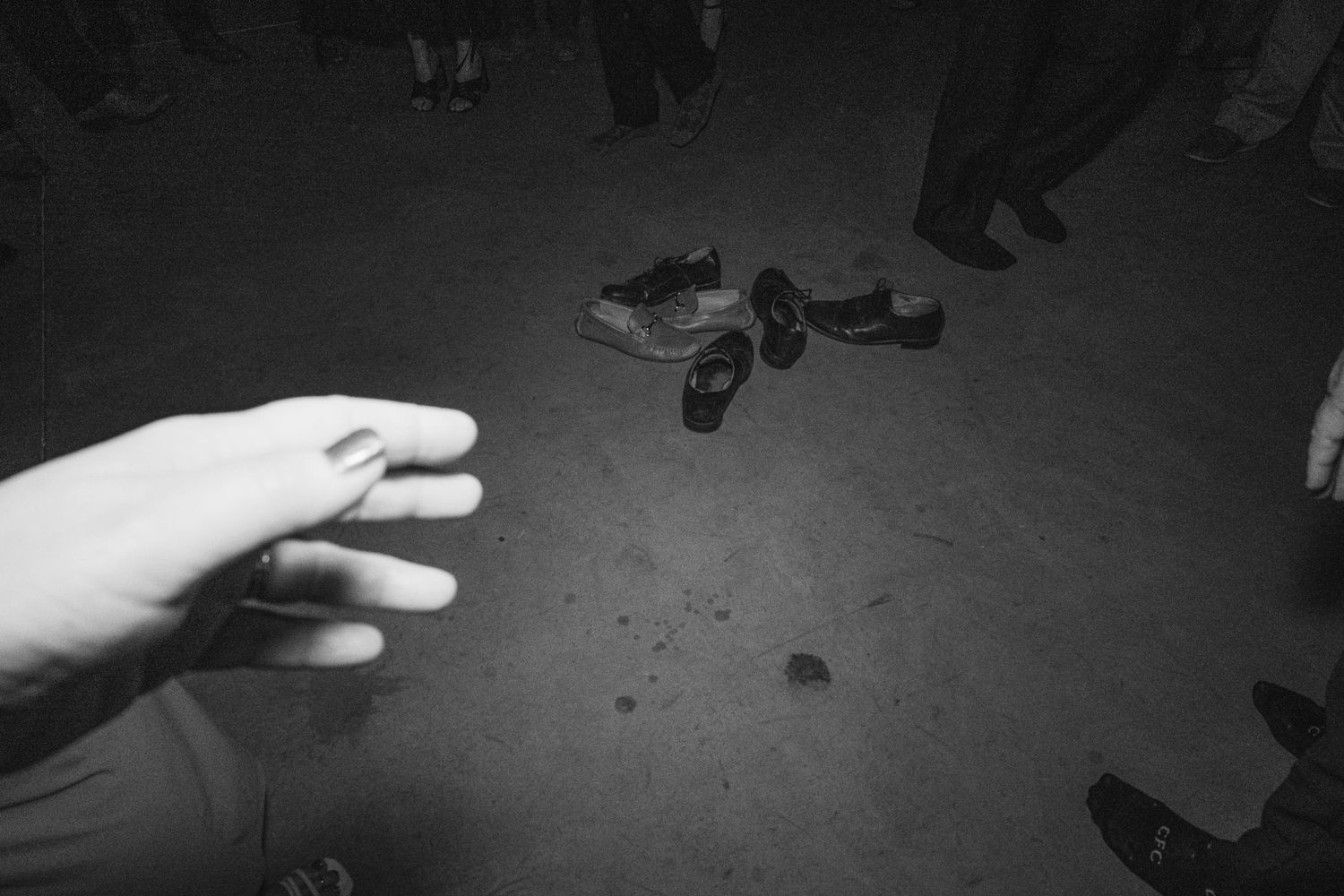 Black and white photo of shoes on ground surrounded by people's feet at a nighttime outdoor gathering.