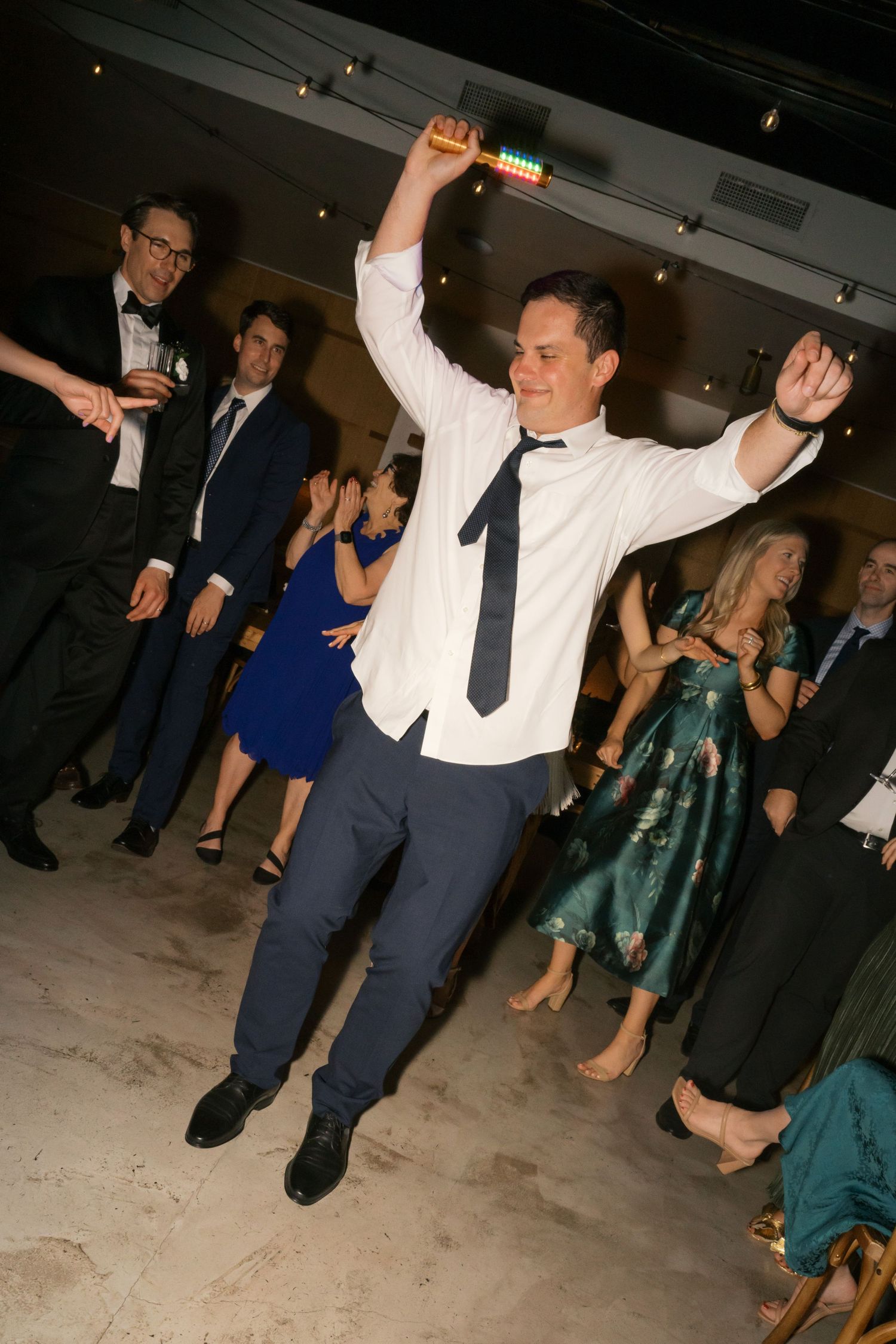 Guest dances energetically on the dance floor during a formal event with other partygoers in the background.
