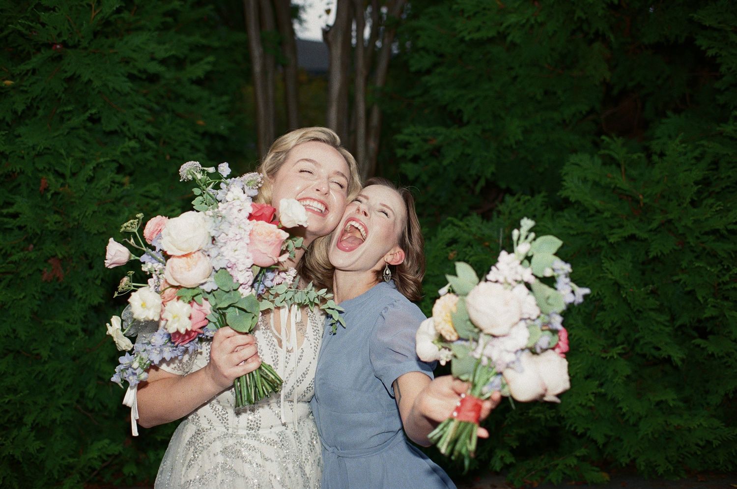 Two people holding floral bouquets express joy and laughter in a garden setting.