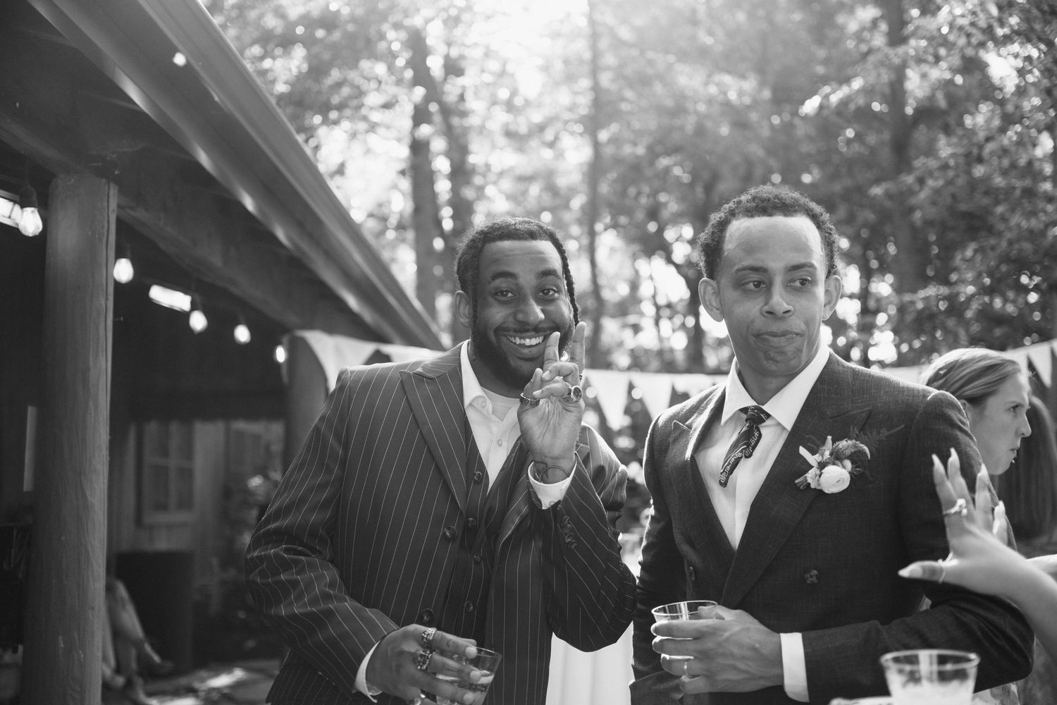 Two men in suits share a laugh at an outdoor celebration.