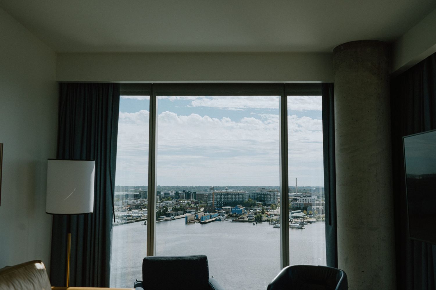 A modern hotel room window offers a panoramic view of a waterfront cityscape.