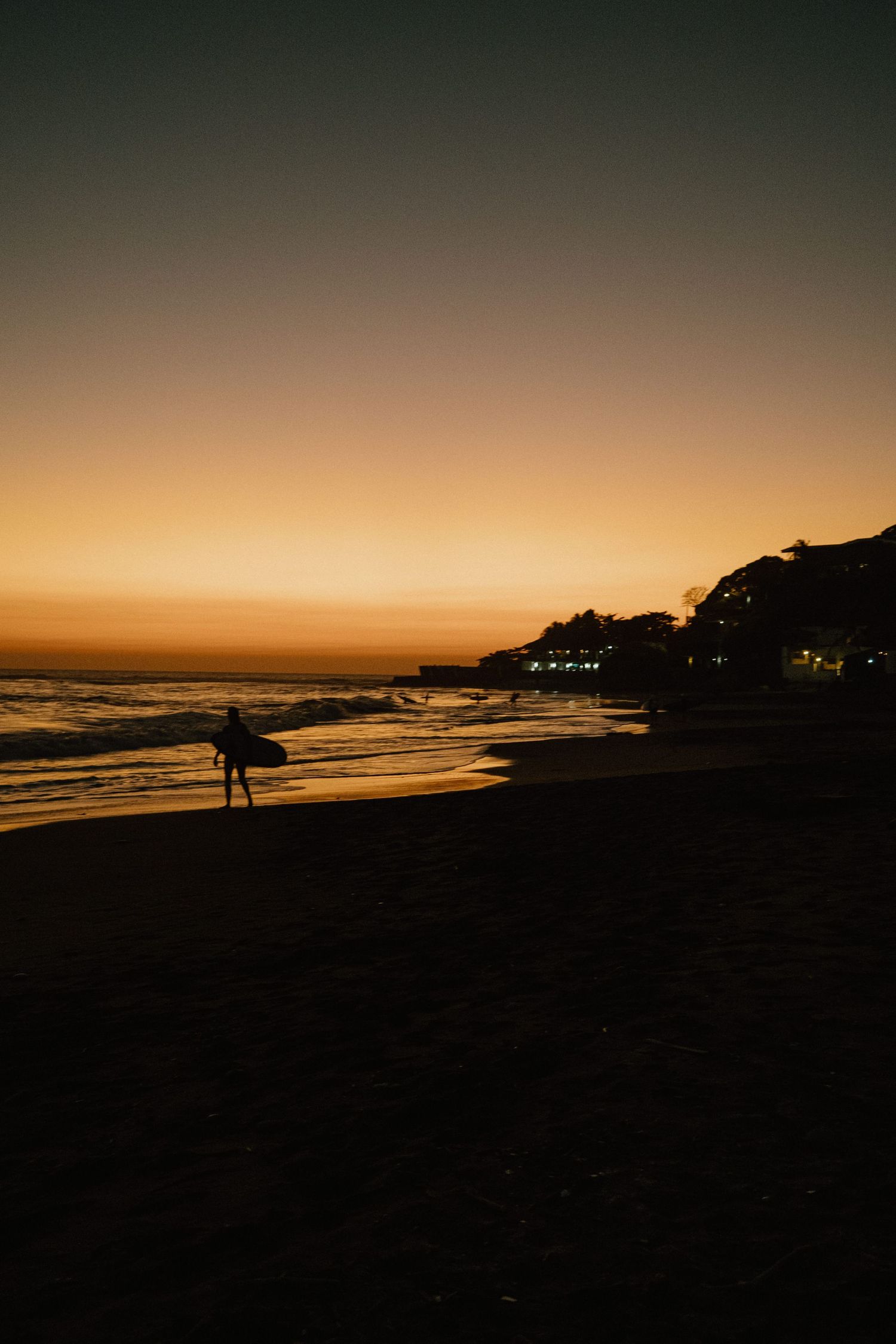 Silhouette of a surfer walking along beach during golden sunset.