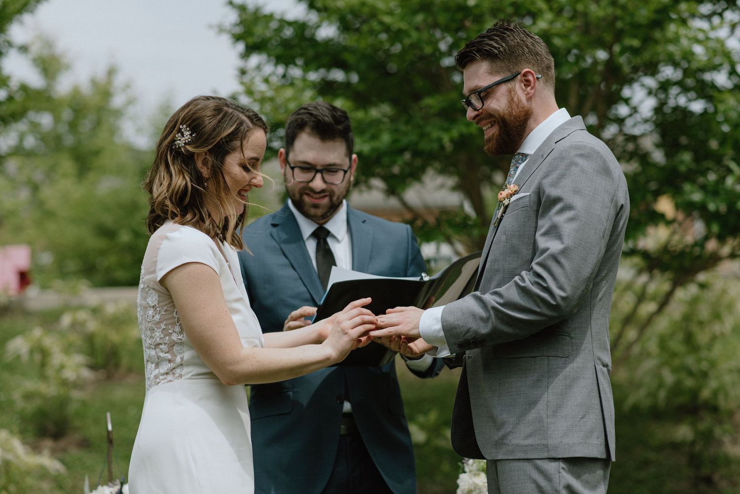 A wedding ceremony takes place outdoors as rings are exchanged during the vows.