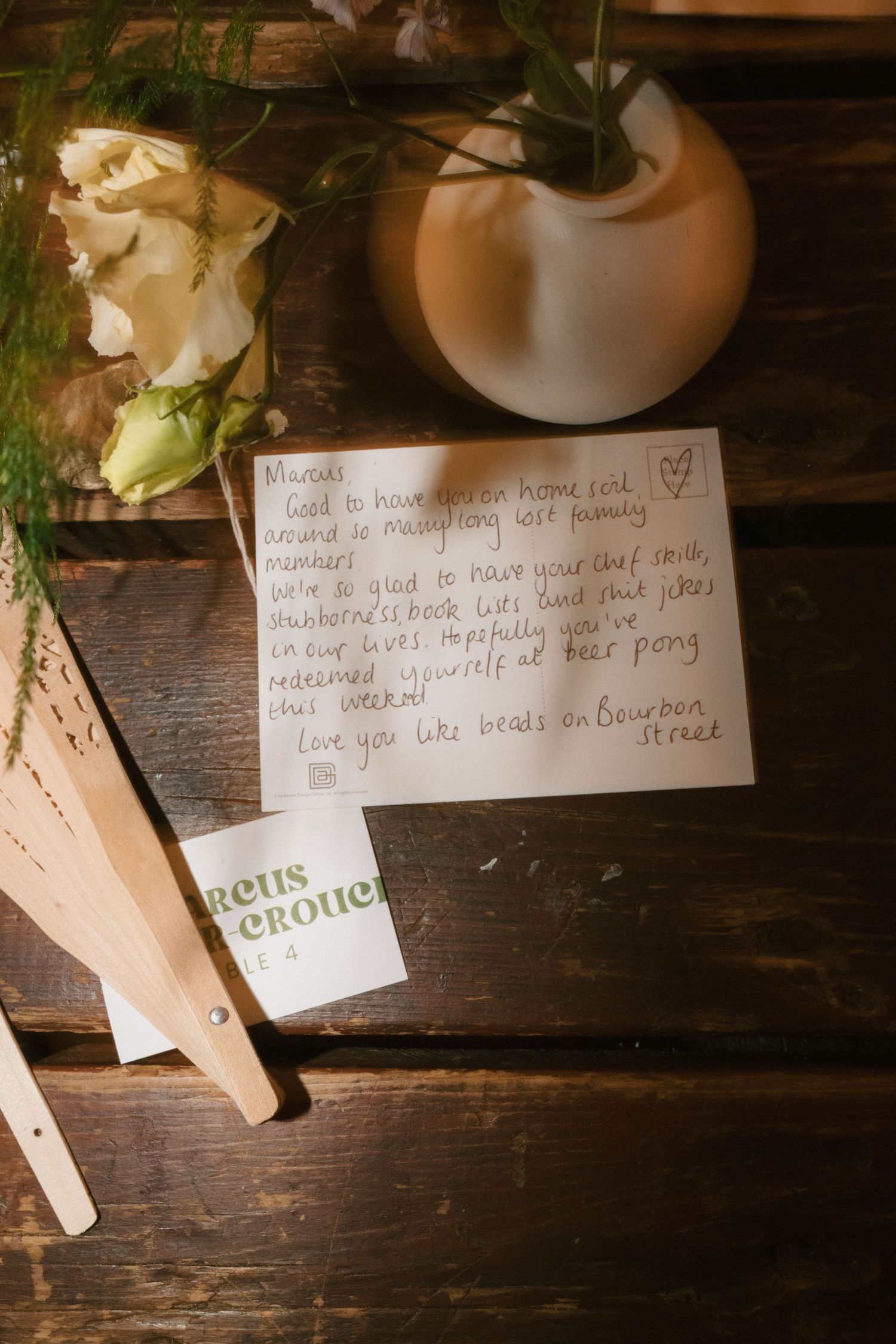 Handwritten note and floral arrangement on wooden surface with decorative elements.