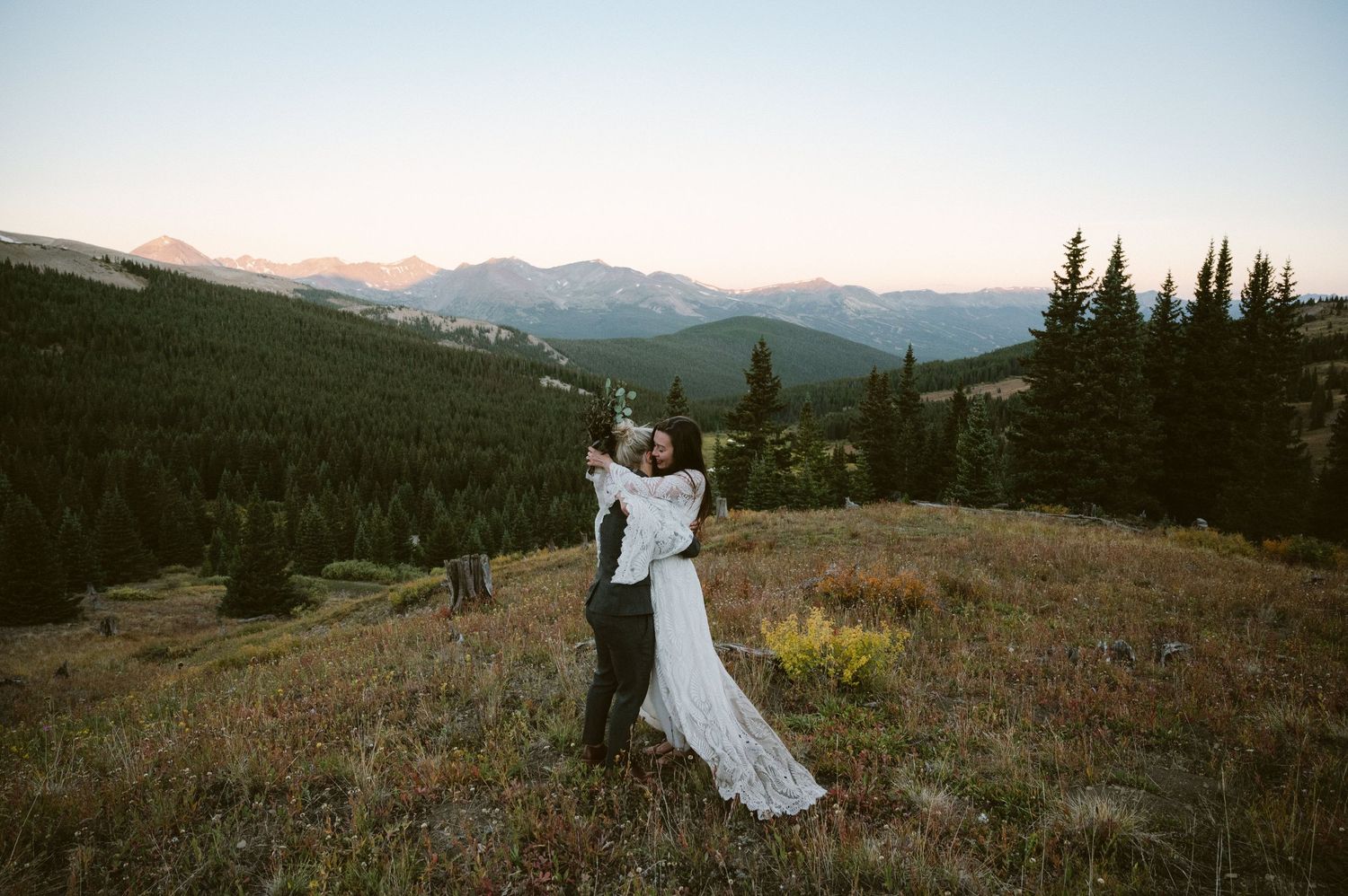 A couple embracing on a mountain overlook with vast forest views below.