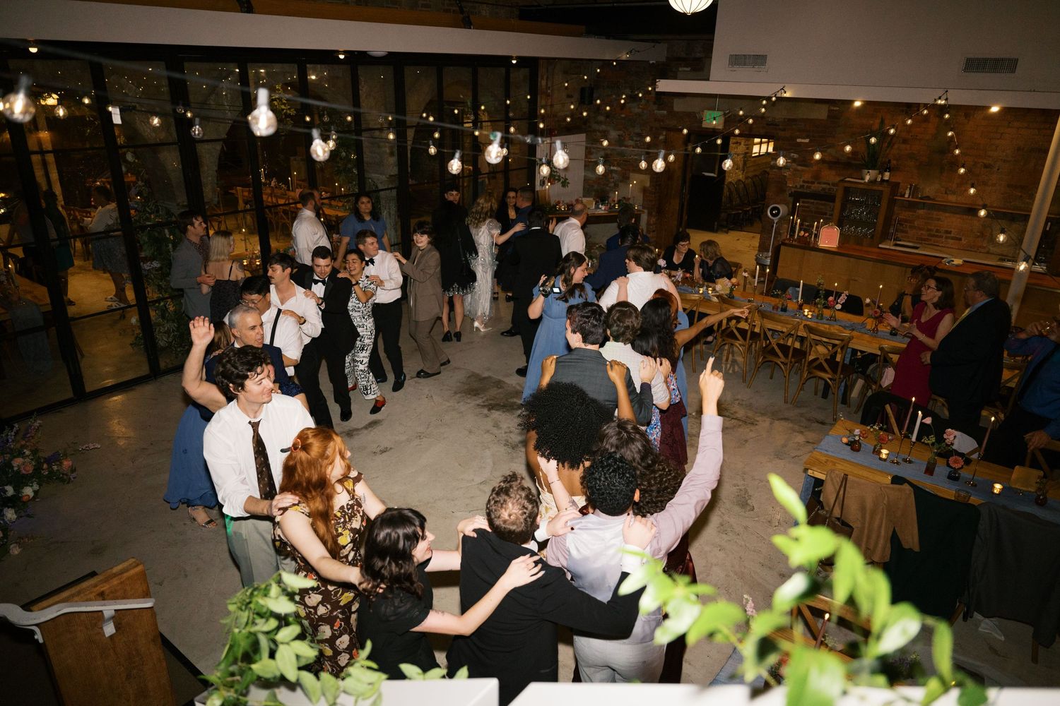 An energetic wedding reception with guests dancing and mingling under string lights.