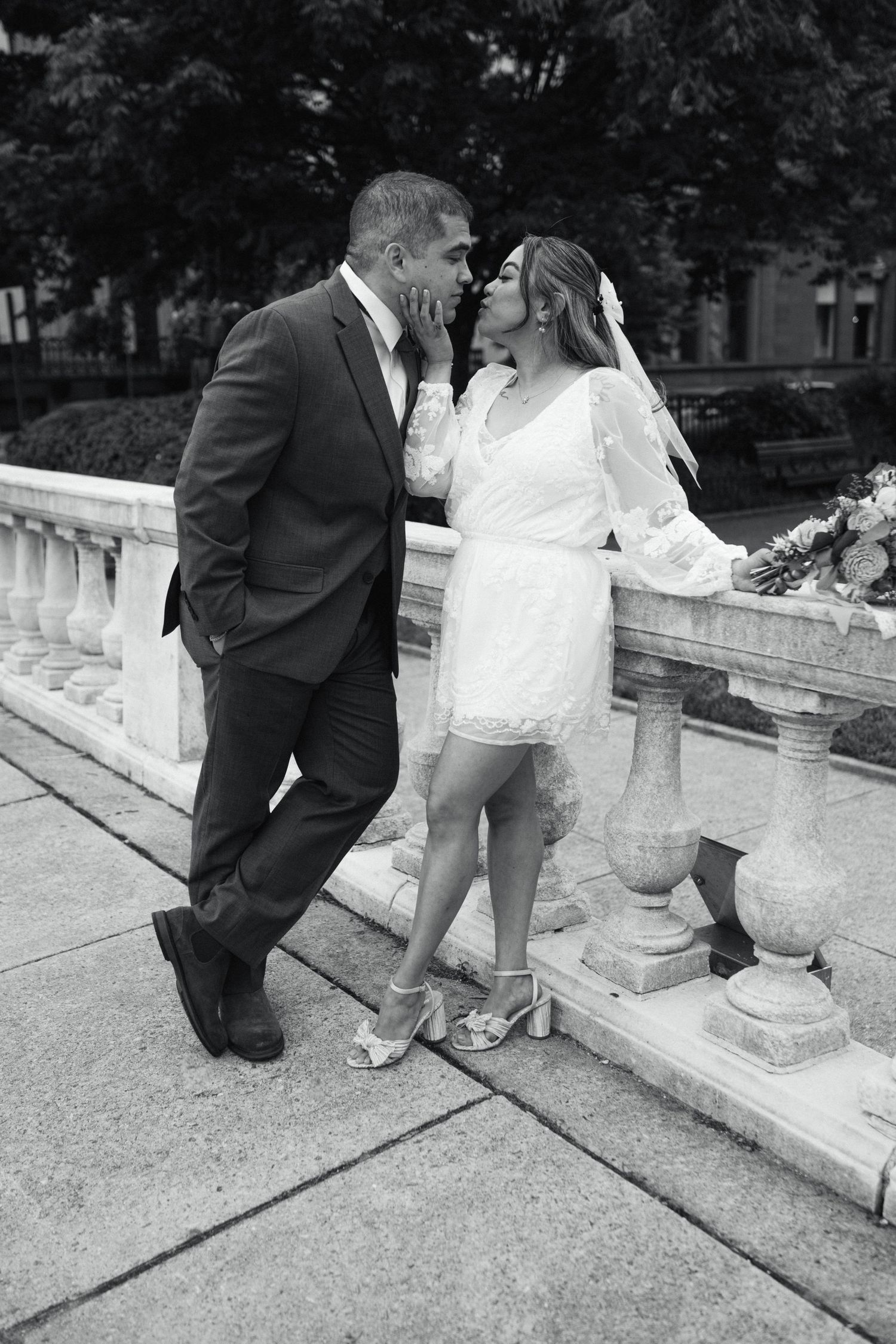 A romantic black and white wedding photo of a couple sharing an intimate moment on stone steps surrounded by greenery.