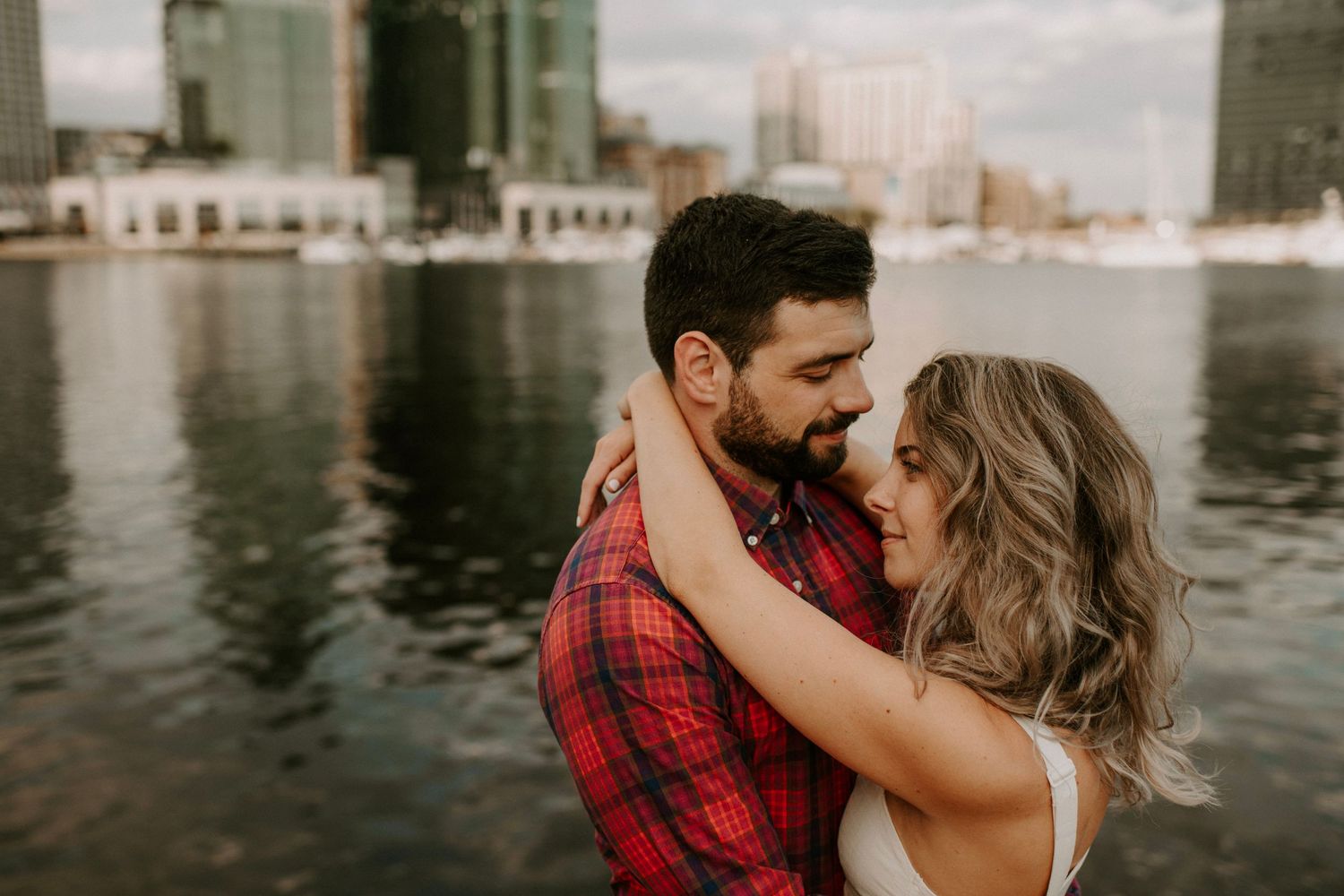 Couple in romantic pose against waterfront with city buildings behind them.