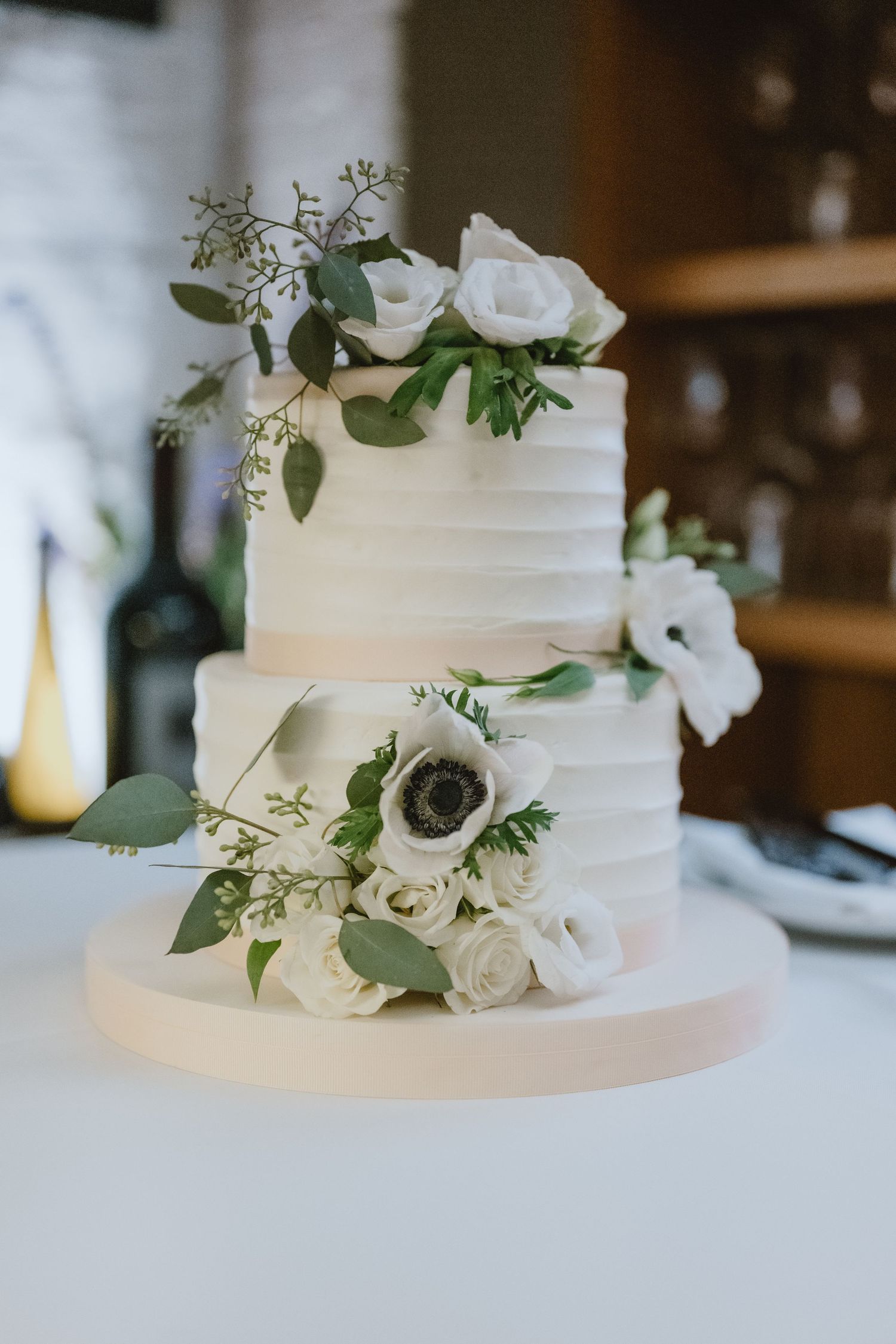 Two-tiered white wedding cake decorated with fresh roses and greenery.