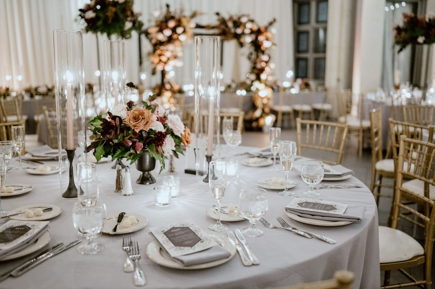 Elegant table setting with floral centerpiece, crystal glasses, and gold chairs at wedding reception.