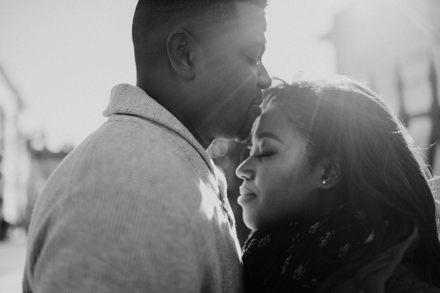 A black and white intimate portrait of a couple sharing a tender romantic moment in natural light.