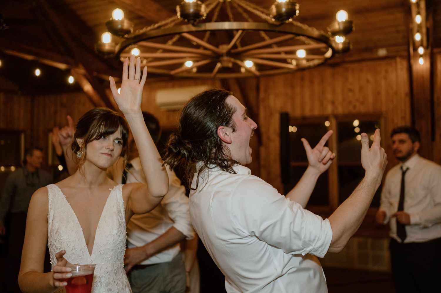 Wedding celebration with enthusiastic dancing under rustic wooden beams and chandeliers.