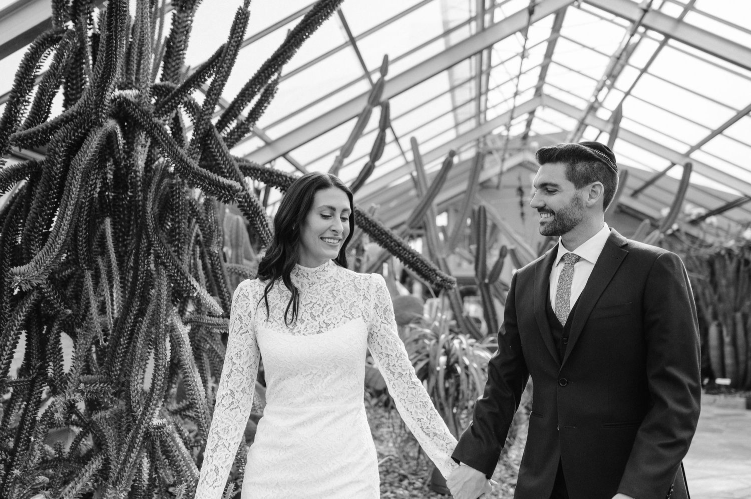 Black and white photo of a couple walking through a greenhouse filled with cacti and tropical plants.