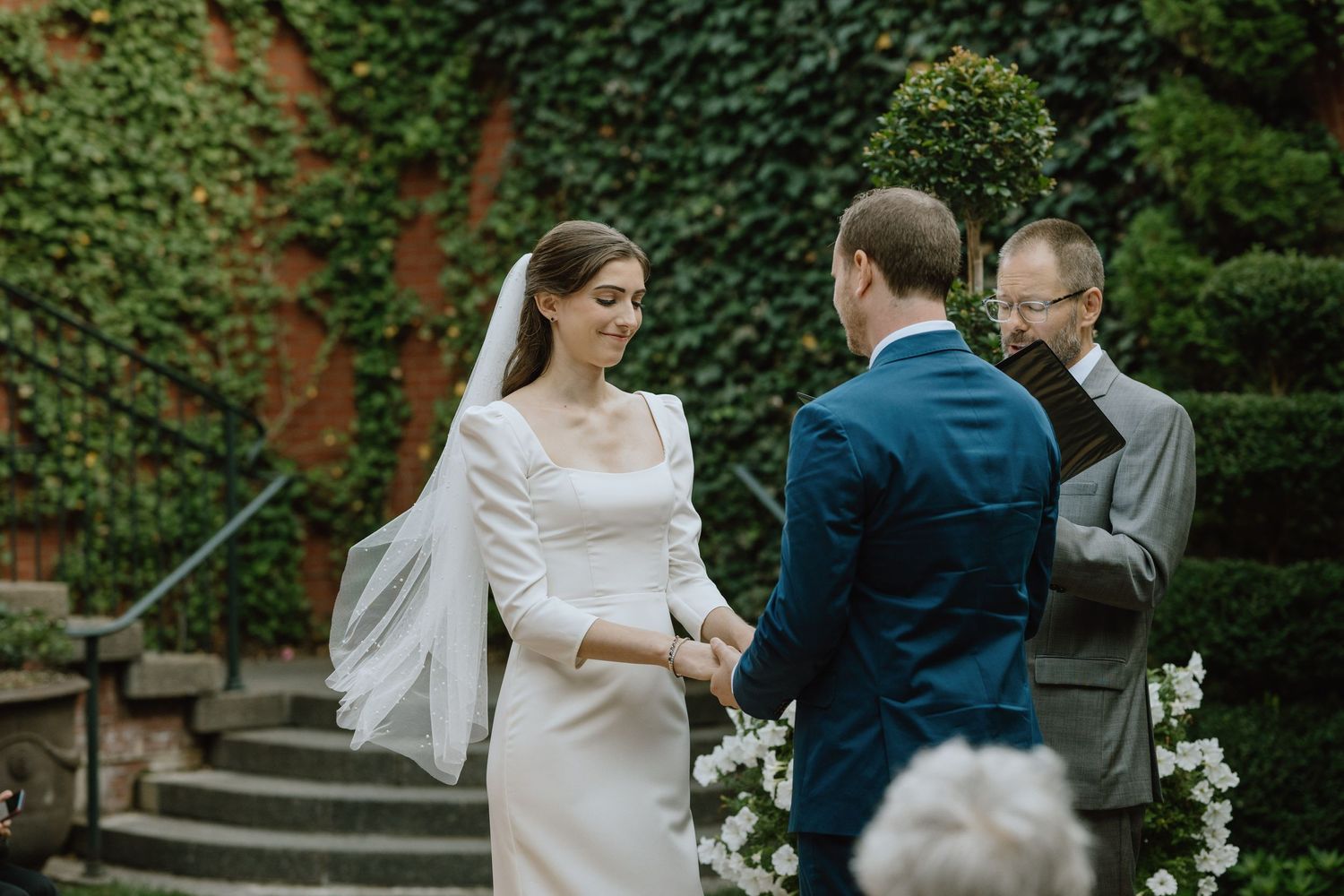 A wedding ceremony unfolds in front of an ivy-covered wall with elegant decorations.