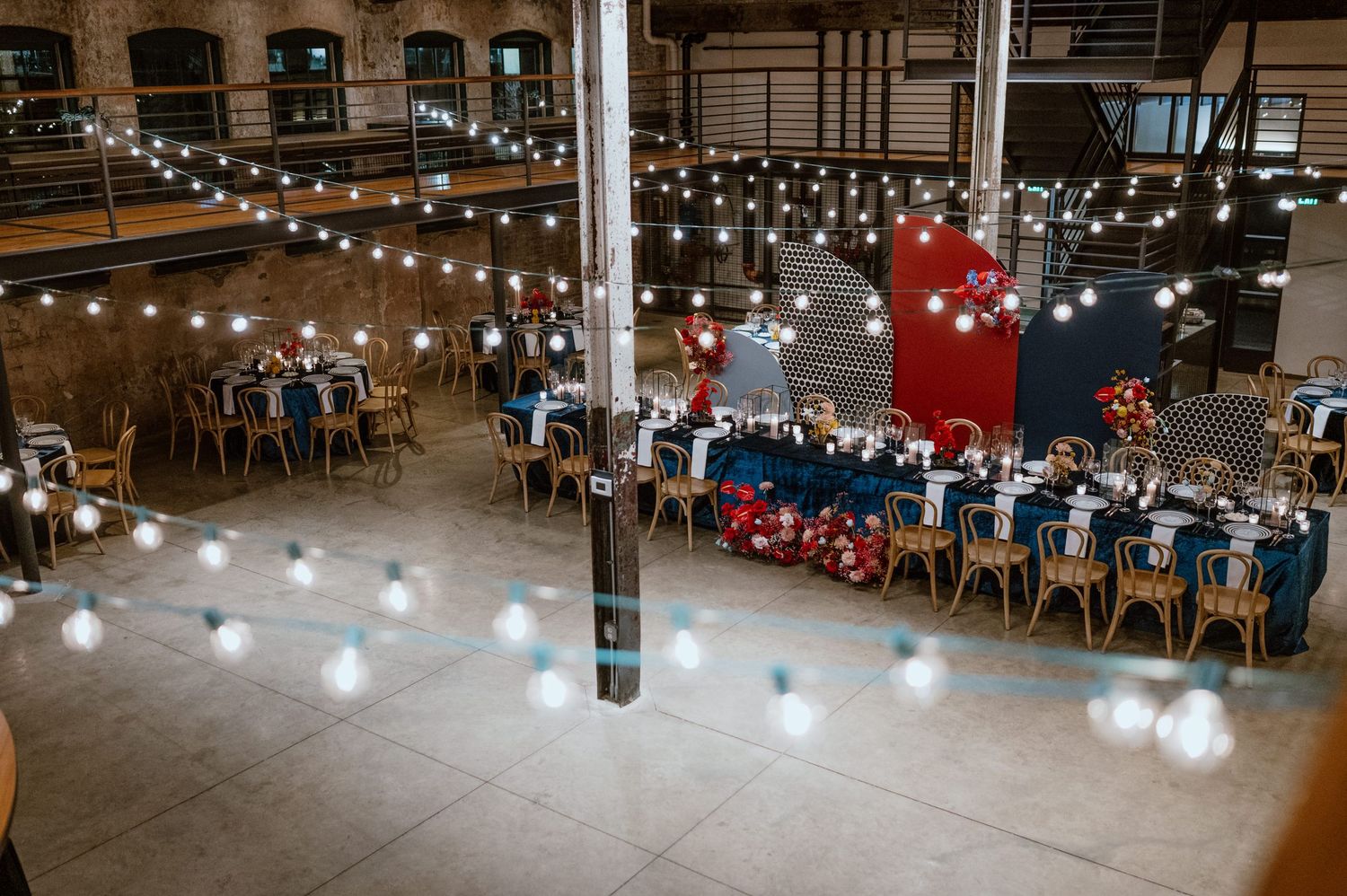 Overhead view of a wedding reception setup with navy and red decor under string lights.