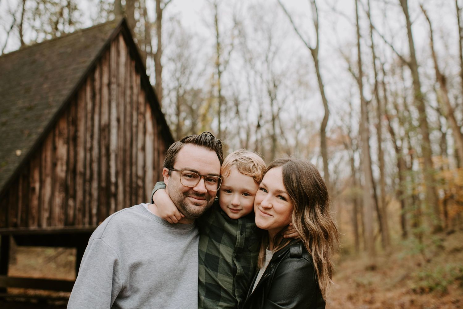 Family posing together in front of rustic wooden building during autumn.