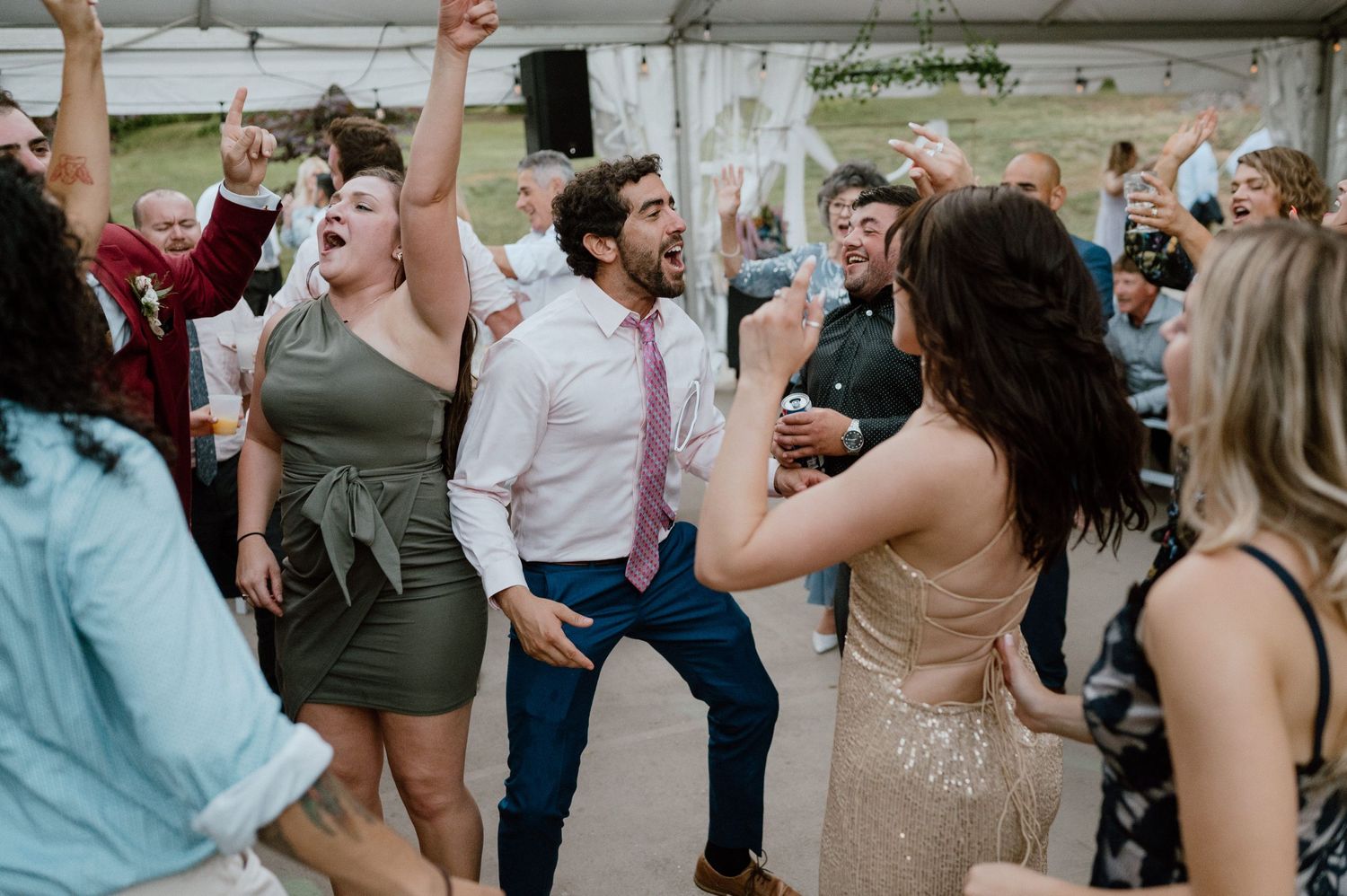 Wedding guests dancing and having fun at an outdoor reception under a white tent.