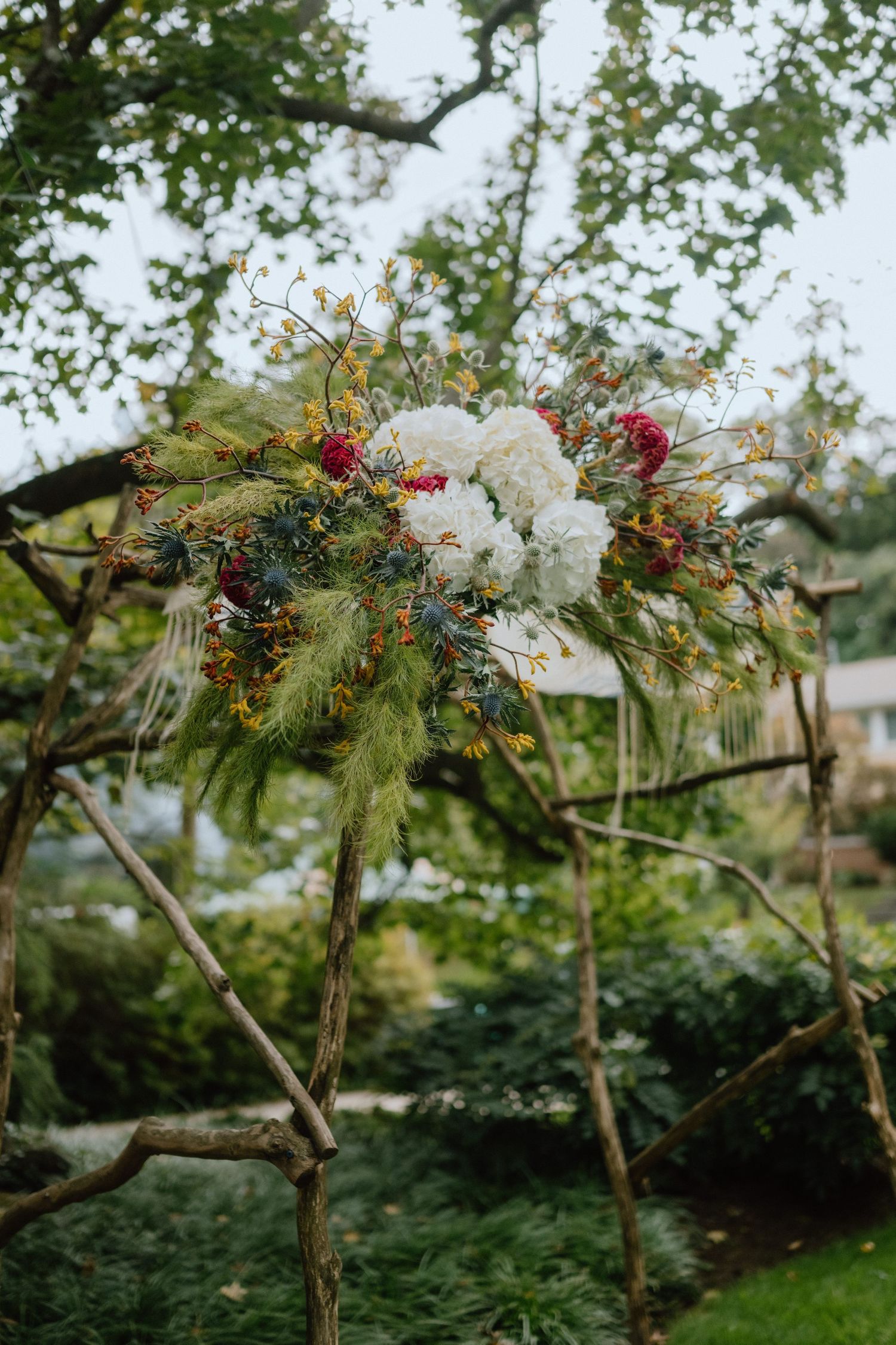 Elegant floral arrangement with white flowers and colorful wildflowers mounted on rustic wooden posts.