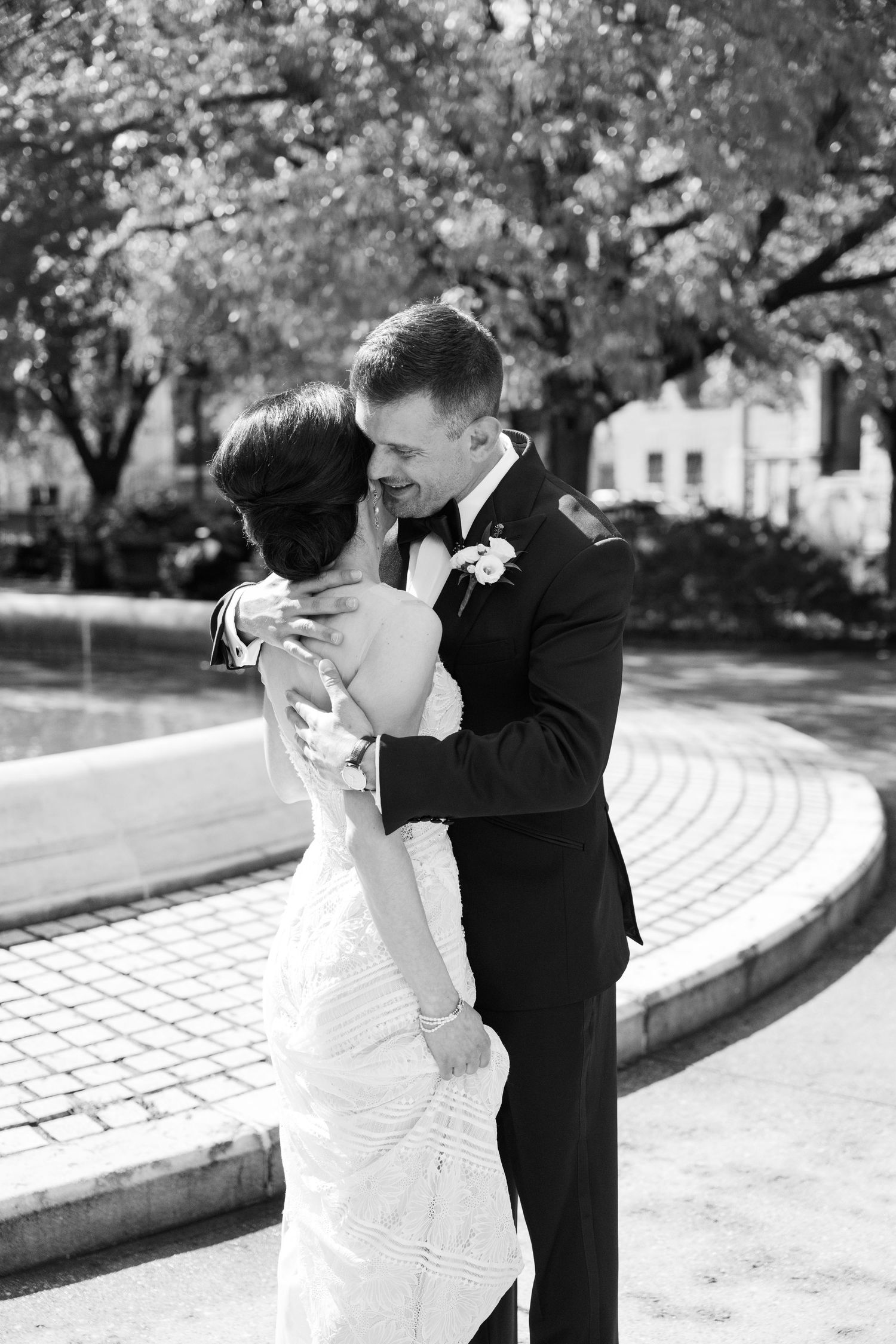 A romantic black and white moment of newlyweds embracing outdoors in formal attire.