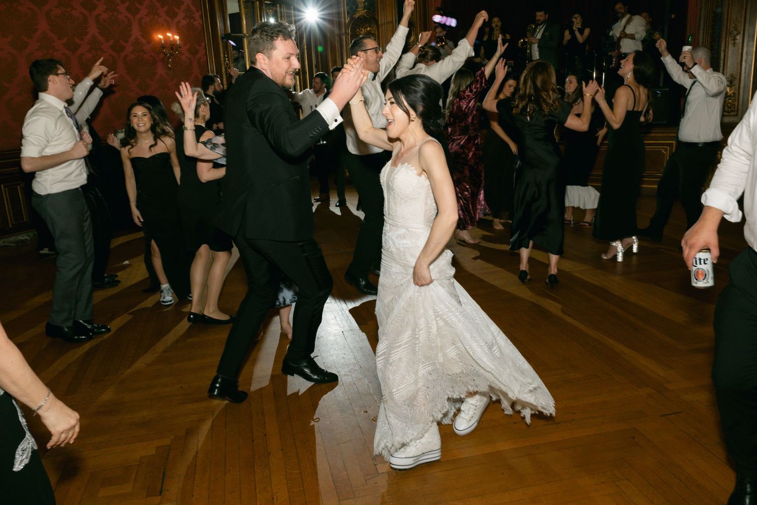Lively wedding dance floor scene with guests celebrating in an ornate ballroom setting.