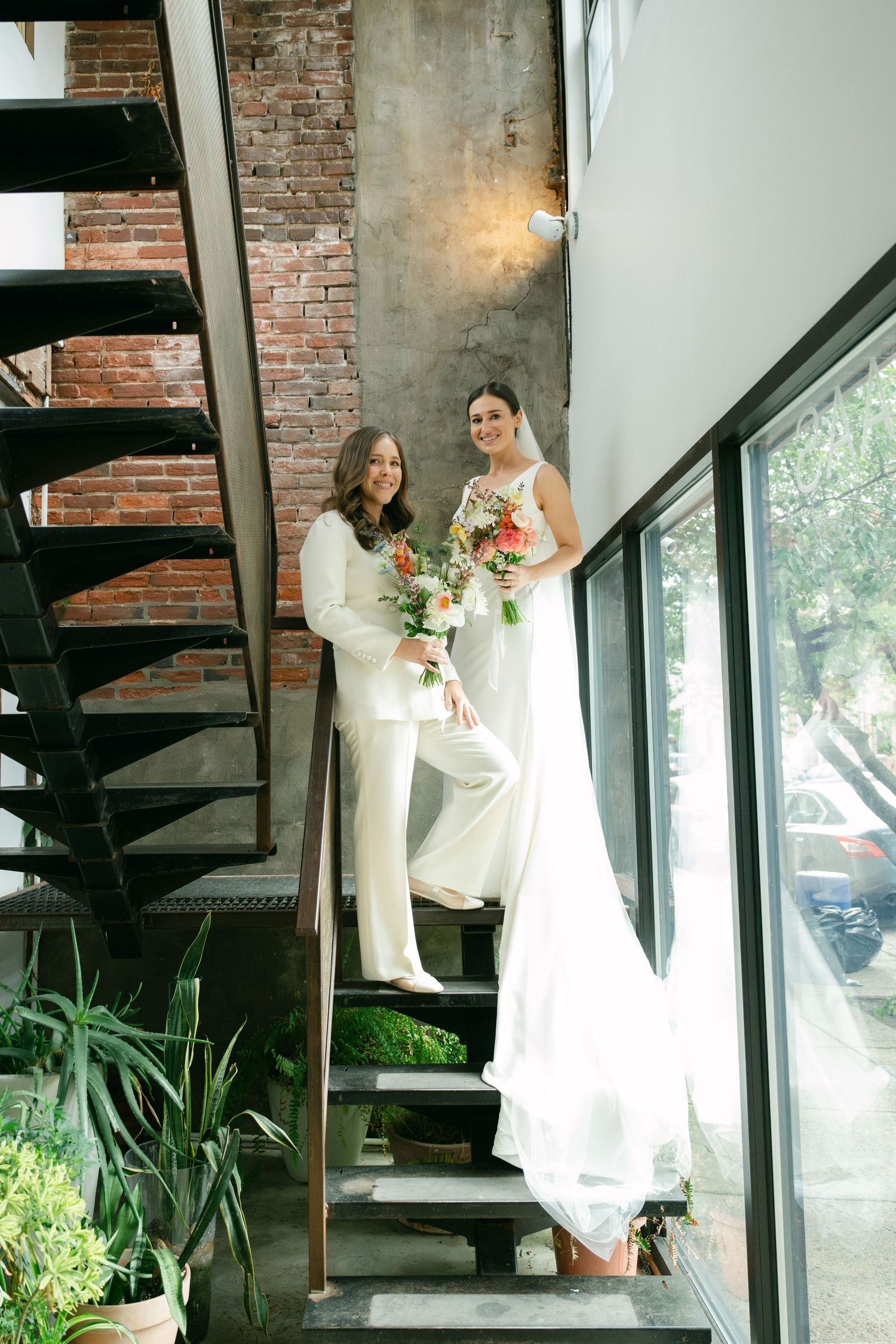 Wedding party ascending modern industrial staircase with exposed brick walls and large windows.
