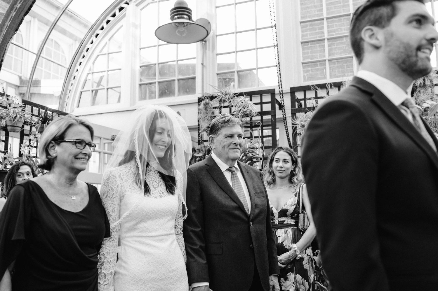 A group of wedding attendees gather in an elegant glass-domed space.