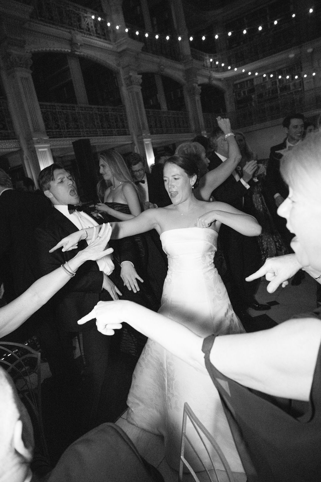 Wedding guests dancing energetically on a crowded dance floor under decorative lighting.