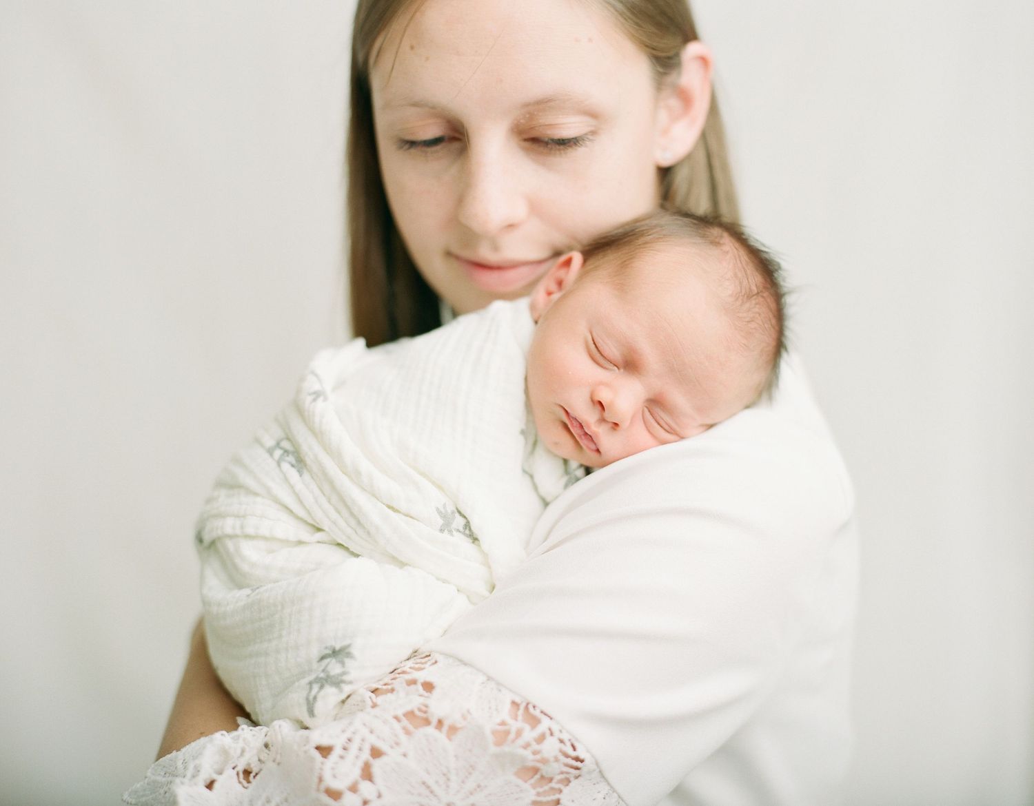 Newborn sleeping on moms shoulder facing camera with a neutral soft background
