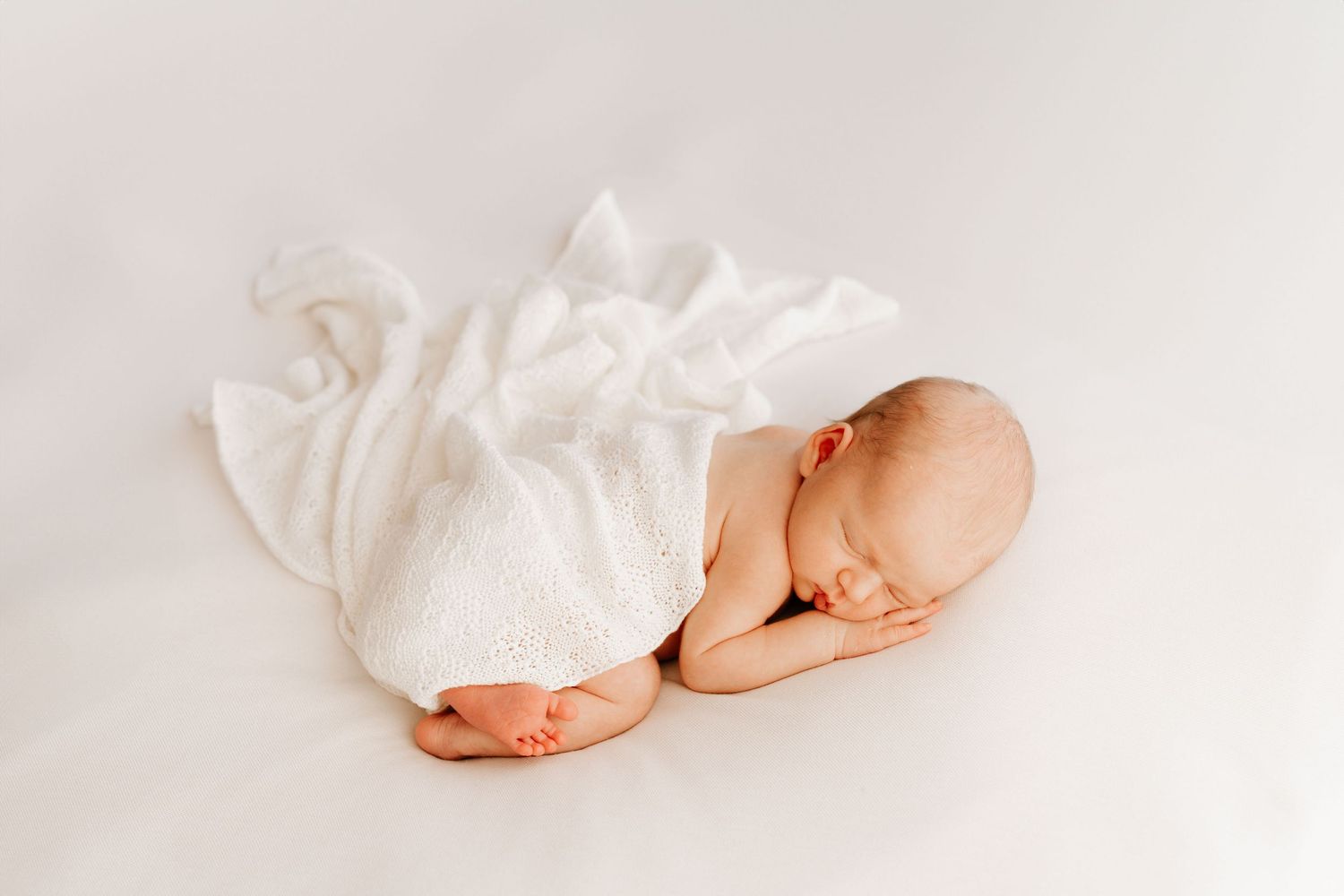 Peaceful newborn baby sleeping wrapped in white lace blanket on white background.