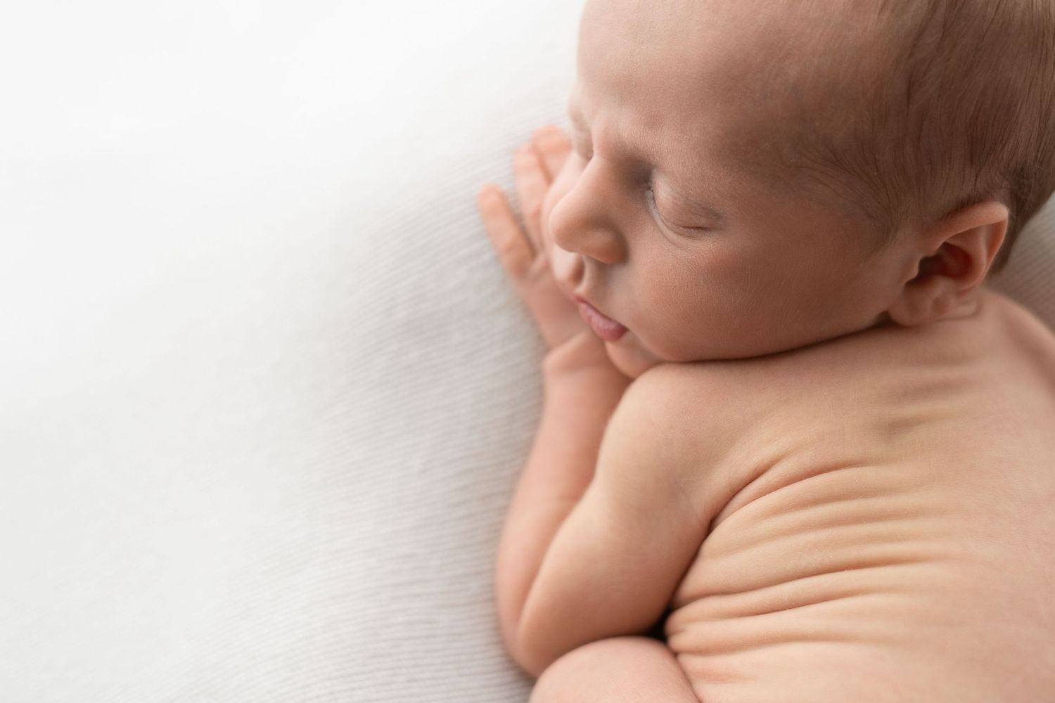Close-up of a sleeping newborn baby lying on a white fluffy blanket with soft natural lighting.