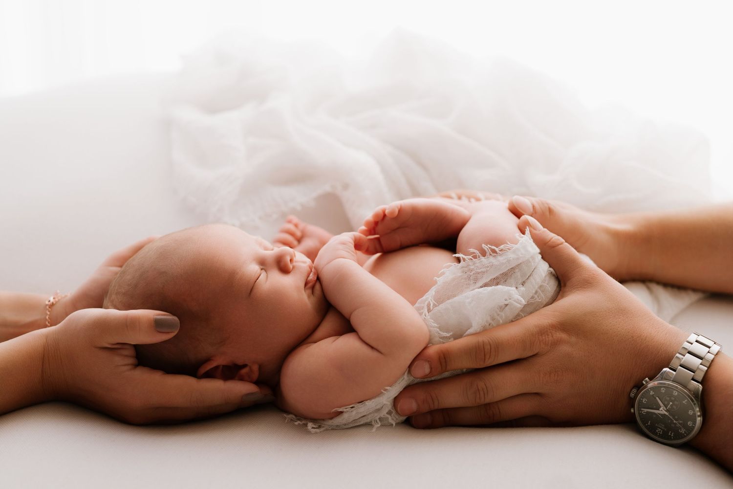 Newborn baby sleeping peacefully while parents gently cradle with loving hands on white background.