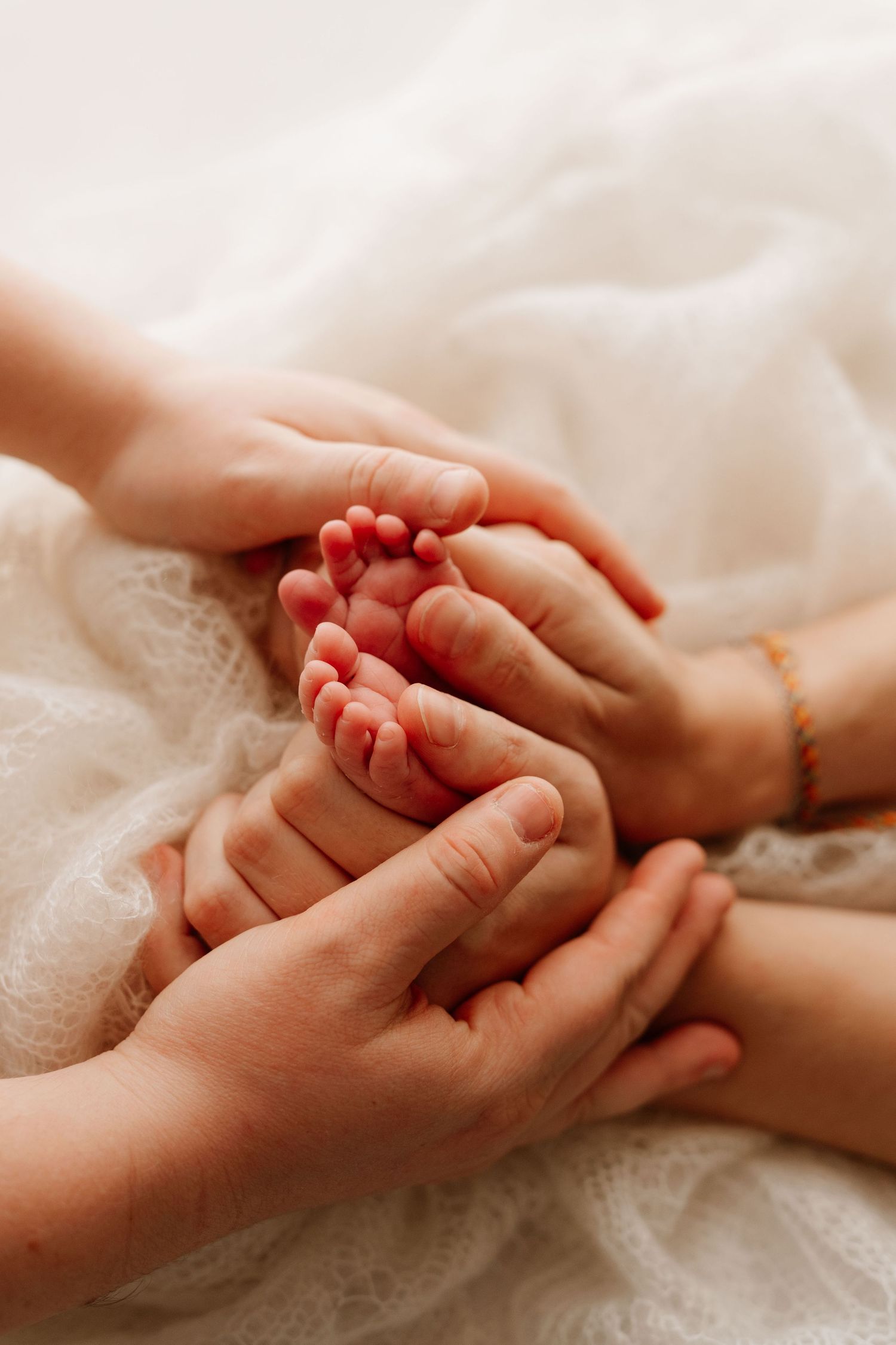 Adult hands gently cradling tiny newborn baby feet on a soft white blanket, symbolizing family love.