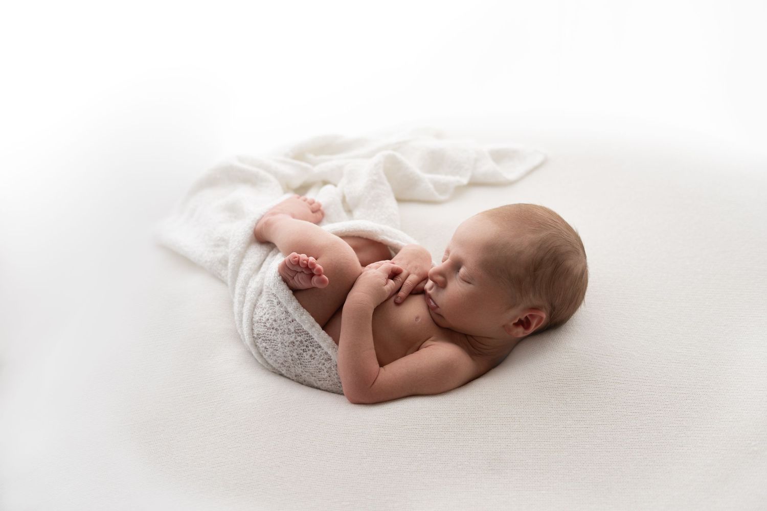 Peaceful newborn baby sleeping curled up on white blanket in professional studio photography.