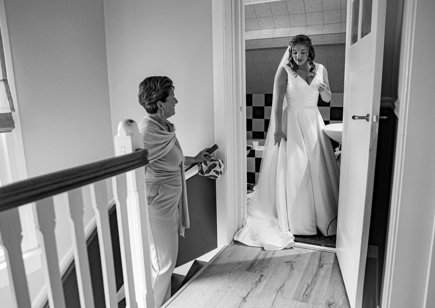 Anticipatory moment as a bride in white gown emerges from a doorway on her wedding day. Trouwfotograaf Nederland. Moment voor de bruiloft.