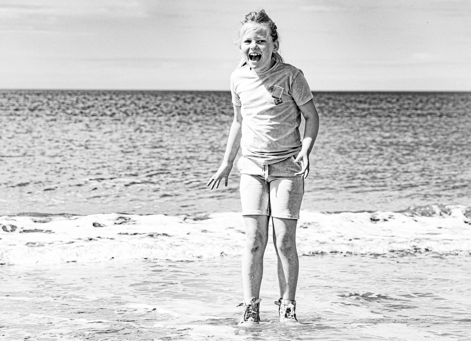 Vintage black and white photograph of a woman standing on a beach. Kindportretten.