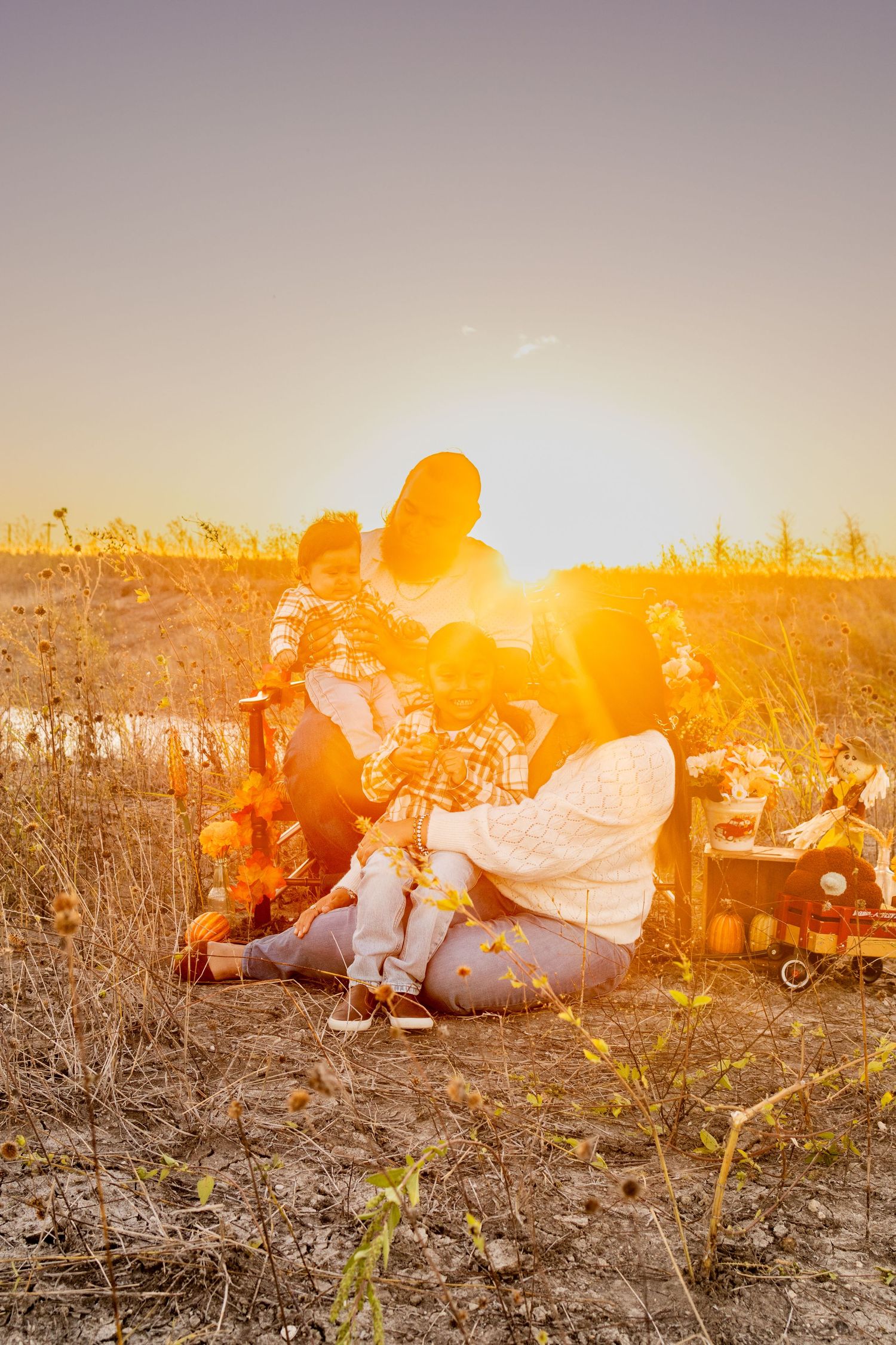 Family sitting together in a field during golden hour sunset with warm orange sunlight creating a dreamy atmosphere.