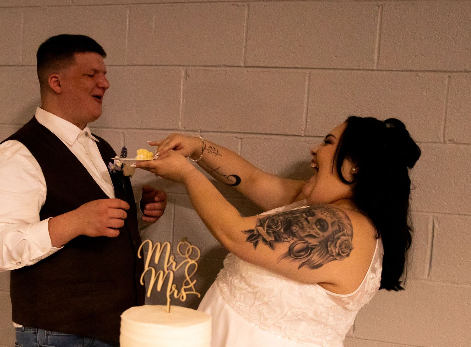 A couple in wedding attire playfully feed each other cake during their wedding reception celebration.