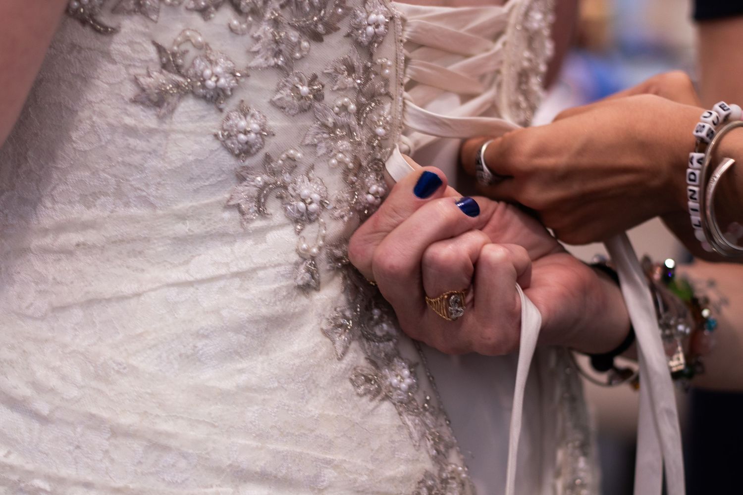 Close-up details of a bride's lace wedding dress being fastened with buttons and ribbons.