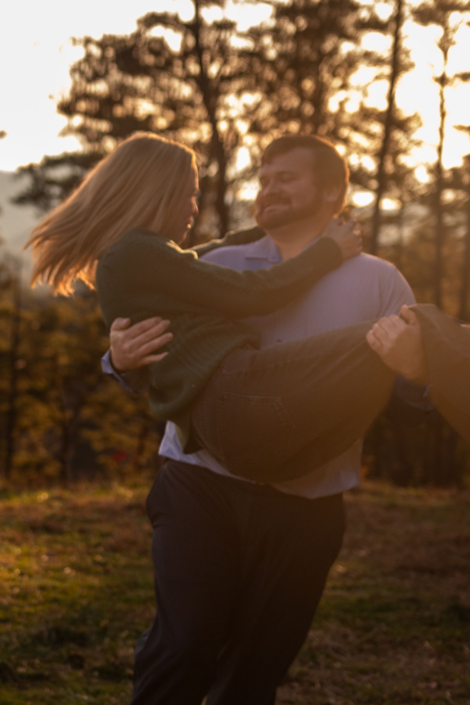 A couple dancing in a romantic sunset embrace with golden light filtering through trees in the background.