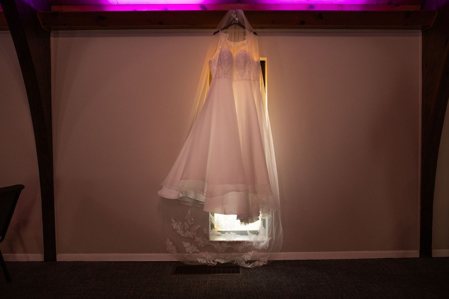 A collection of illuminated wedding dresses displayed on hangers against a dark wall with pink lighting effects.