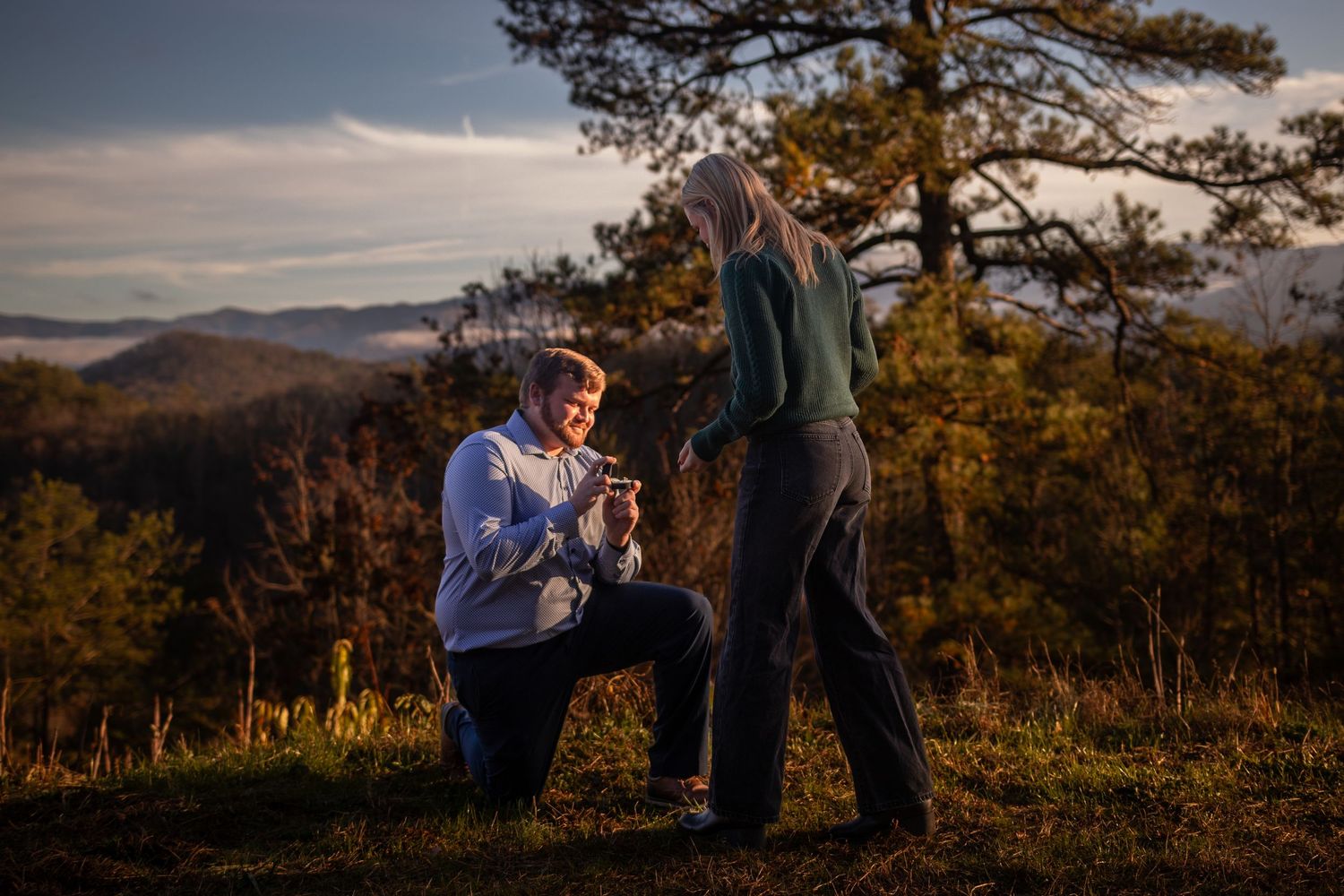 A romantic proposal scene at sunset in the mountains with golden light illuminating a couple among pine trees.