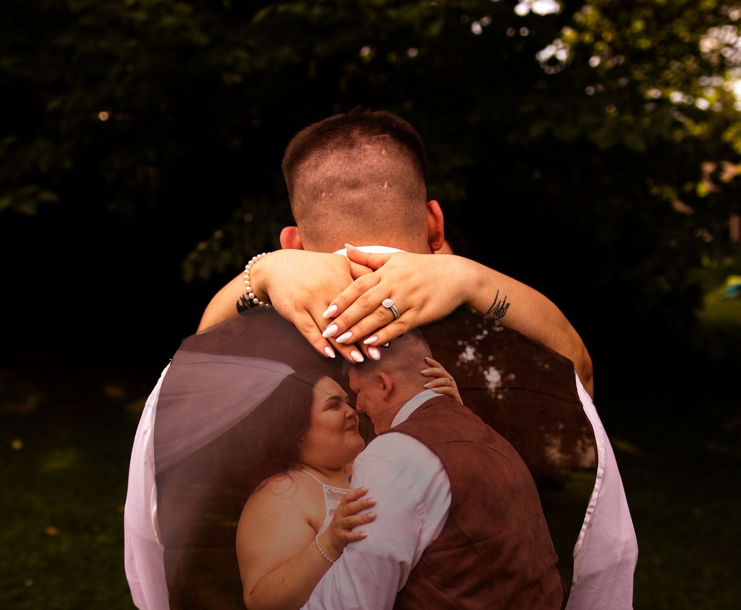A couple embraces in a romantic outdoor setting with sunlight filtering through trees in the background.