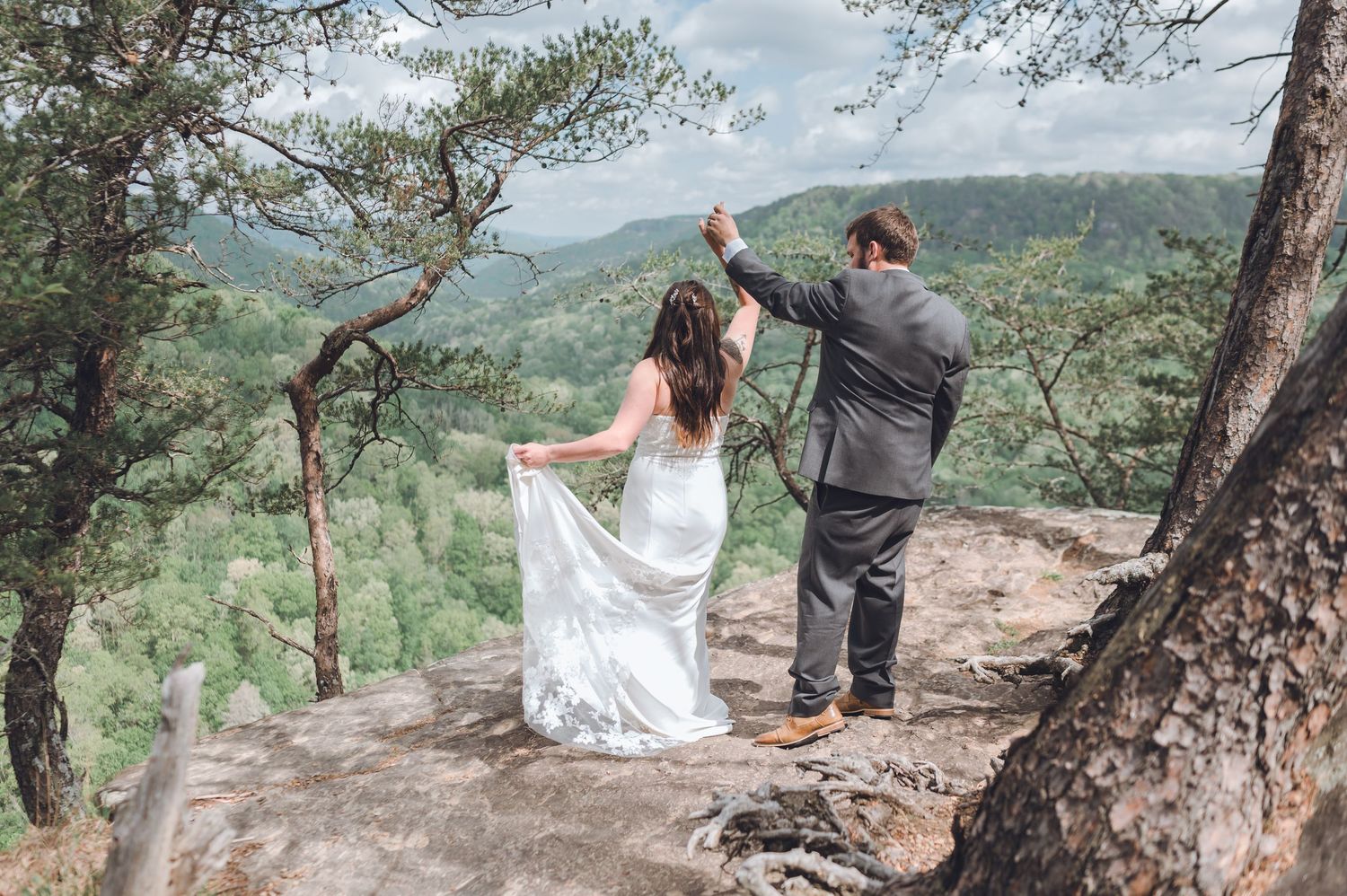 A couple celebrates their wedding day on a scenic mountain overlook surrounded by pine trees and sweeping valley views.