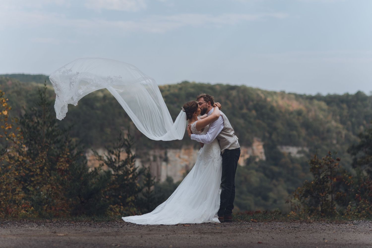 A couple shares an intimate moment during their wedding photoshoot against a scenic mountain backdrop.